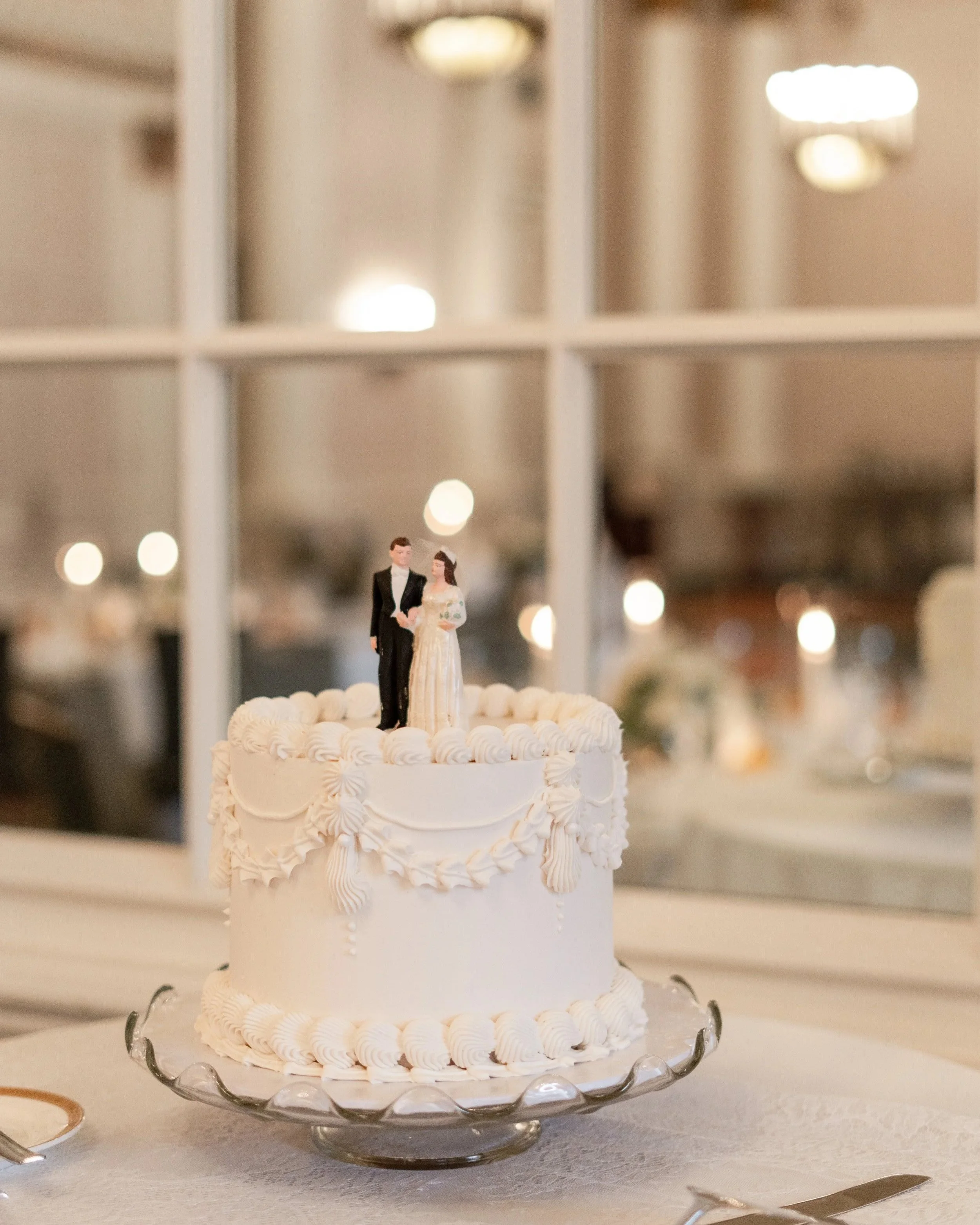 Wedding cake with a bride and groom figurine topper on a glass stand, decorated with white icing. Chateau Laurier, Ottawa, ON