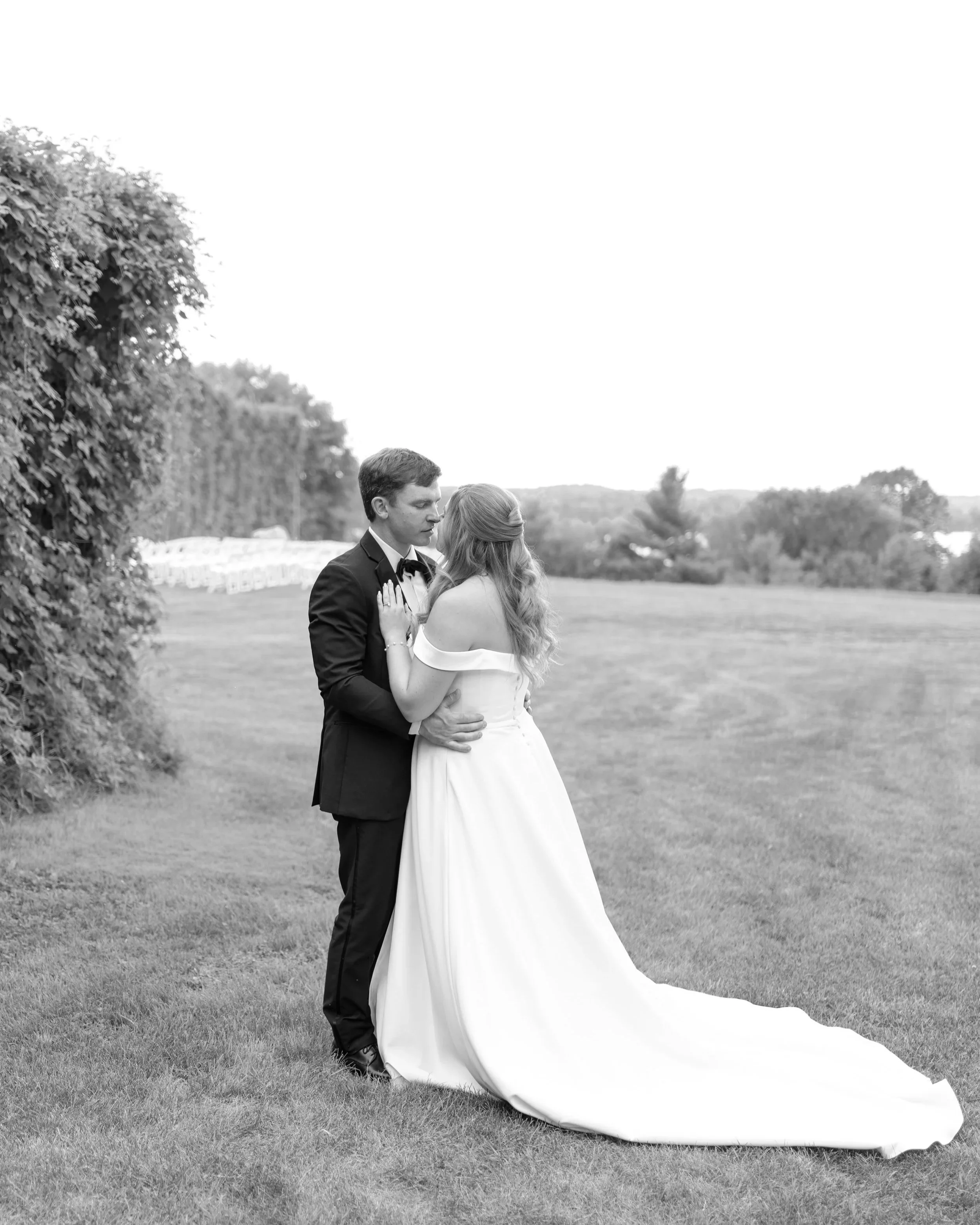 Black and white photo of a bride and groom standing close together on a grassy field, embracing each other during their wedding day. Stone Hedges Hops, Pembroke, ON