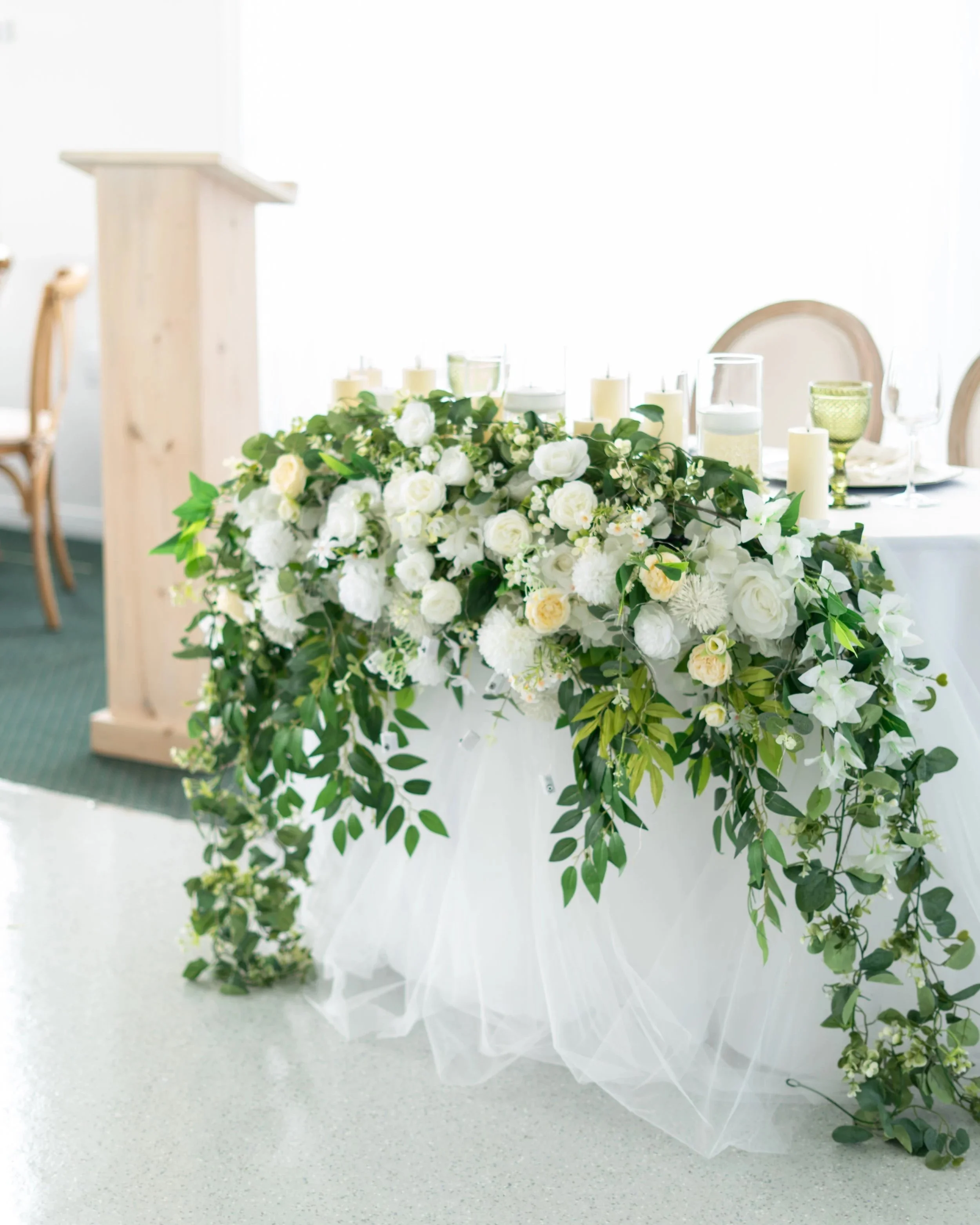 A wedding table decorated with a lush white floral centerpiece and greenery, candles, and glassware. Pembroke Golf Club, Ontario.