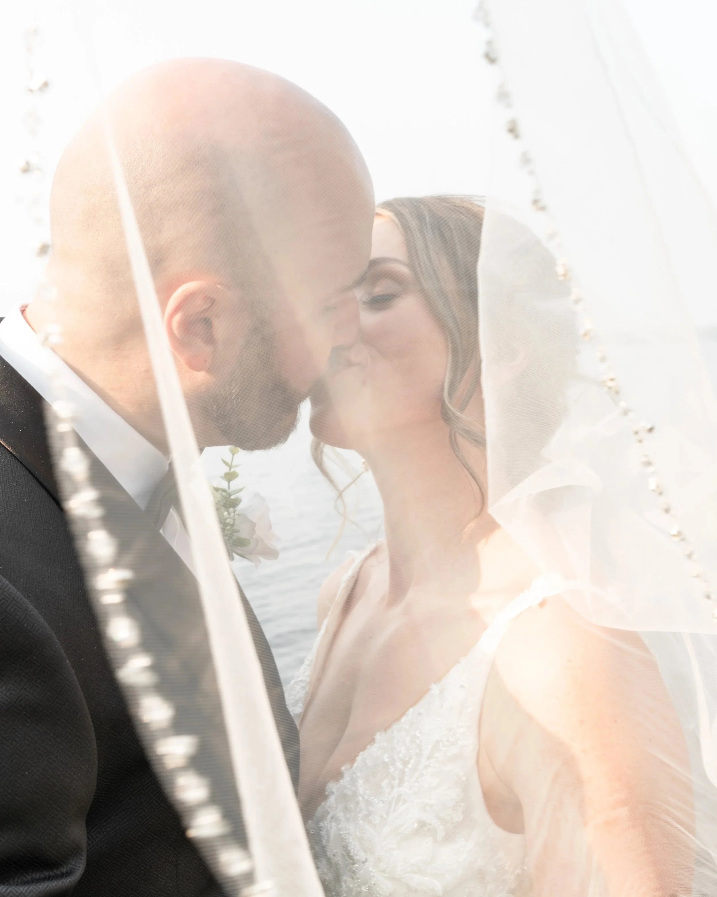 A bride and groom sharing a kiss, seen through a veil, with sunlight creating a lens flare effect. Pembroke wedding