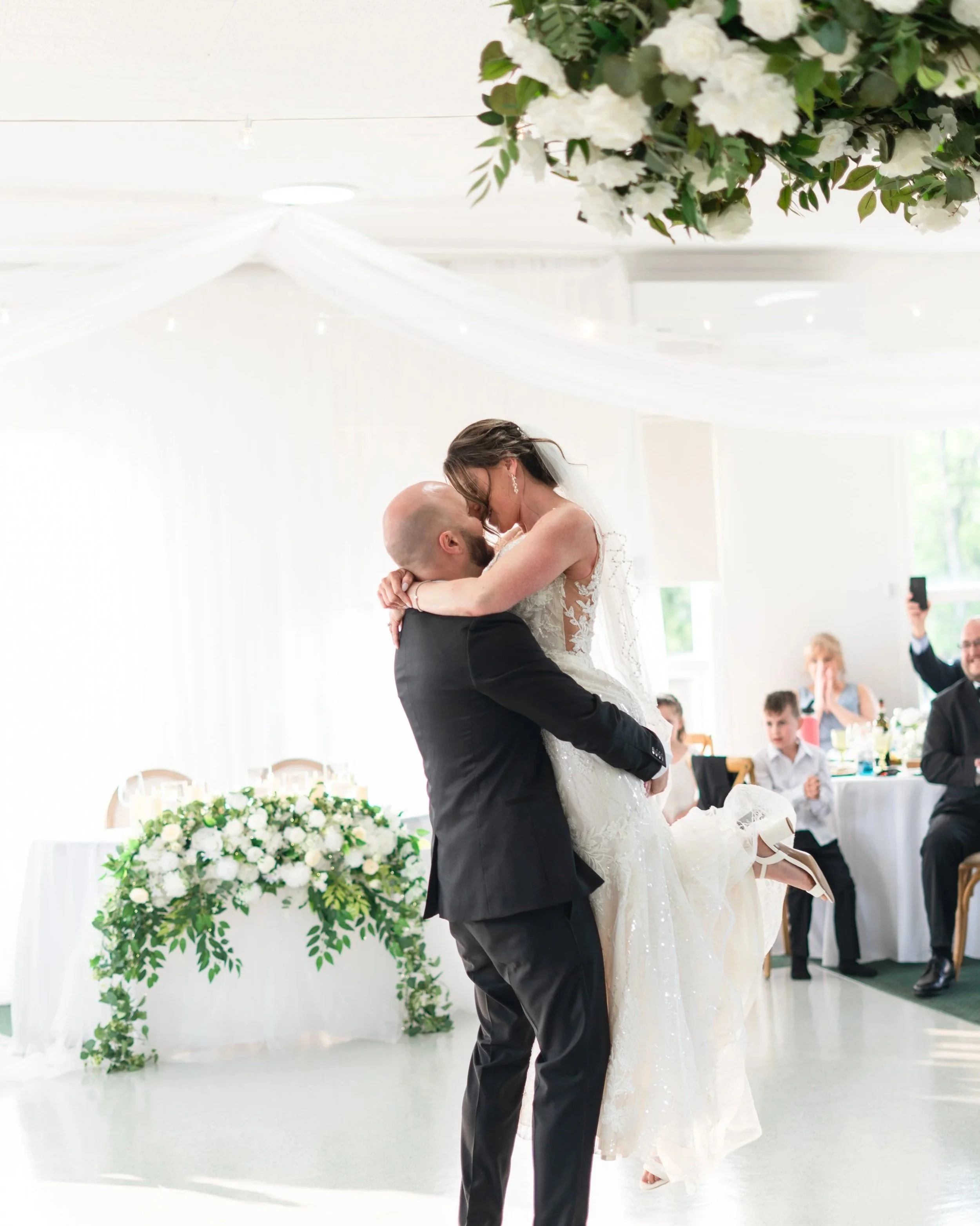A bride and groom share a dance at their wedding reception, with the groom lifting the bride off the ground as she embraces him. Wedding reception at the Pembroke Golf Club in Ontario
