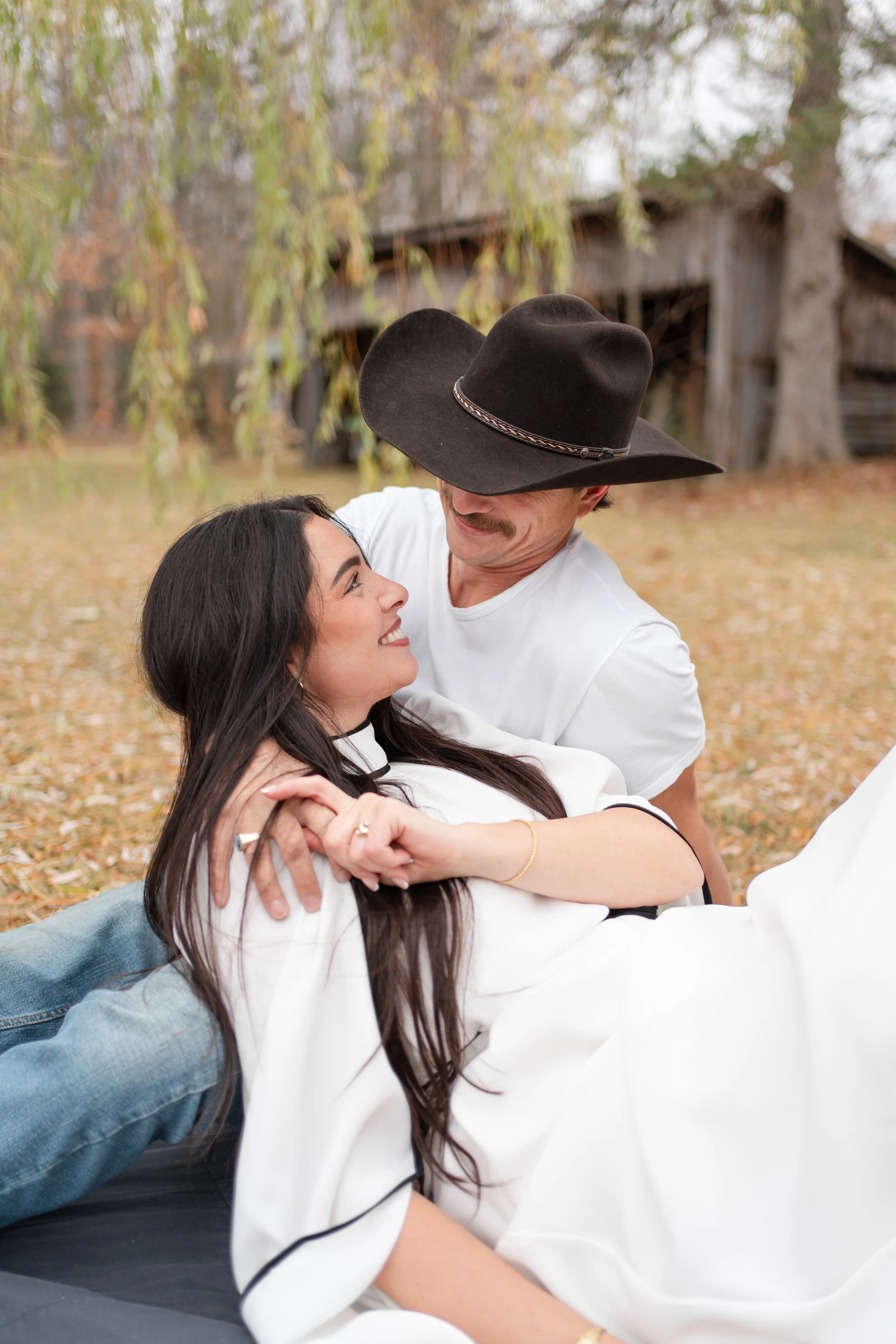 A couple smiling and enjoying each other's company outdoors, with autumn leaves and trees in the background.