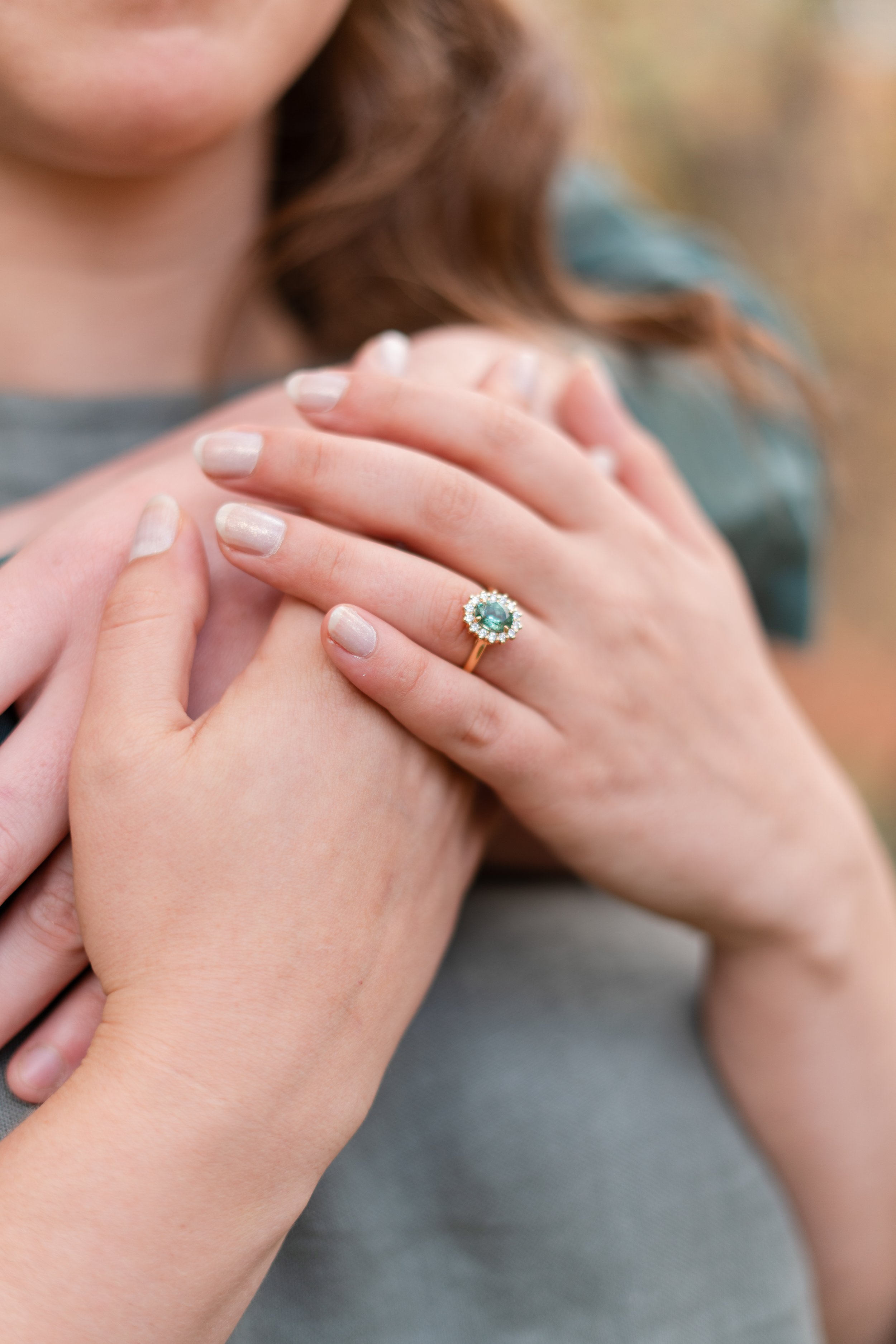 Close-up of two women embracing, one wearing an engagement ring with a large blue gemstone surrounded by diamonds.