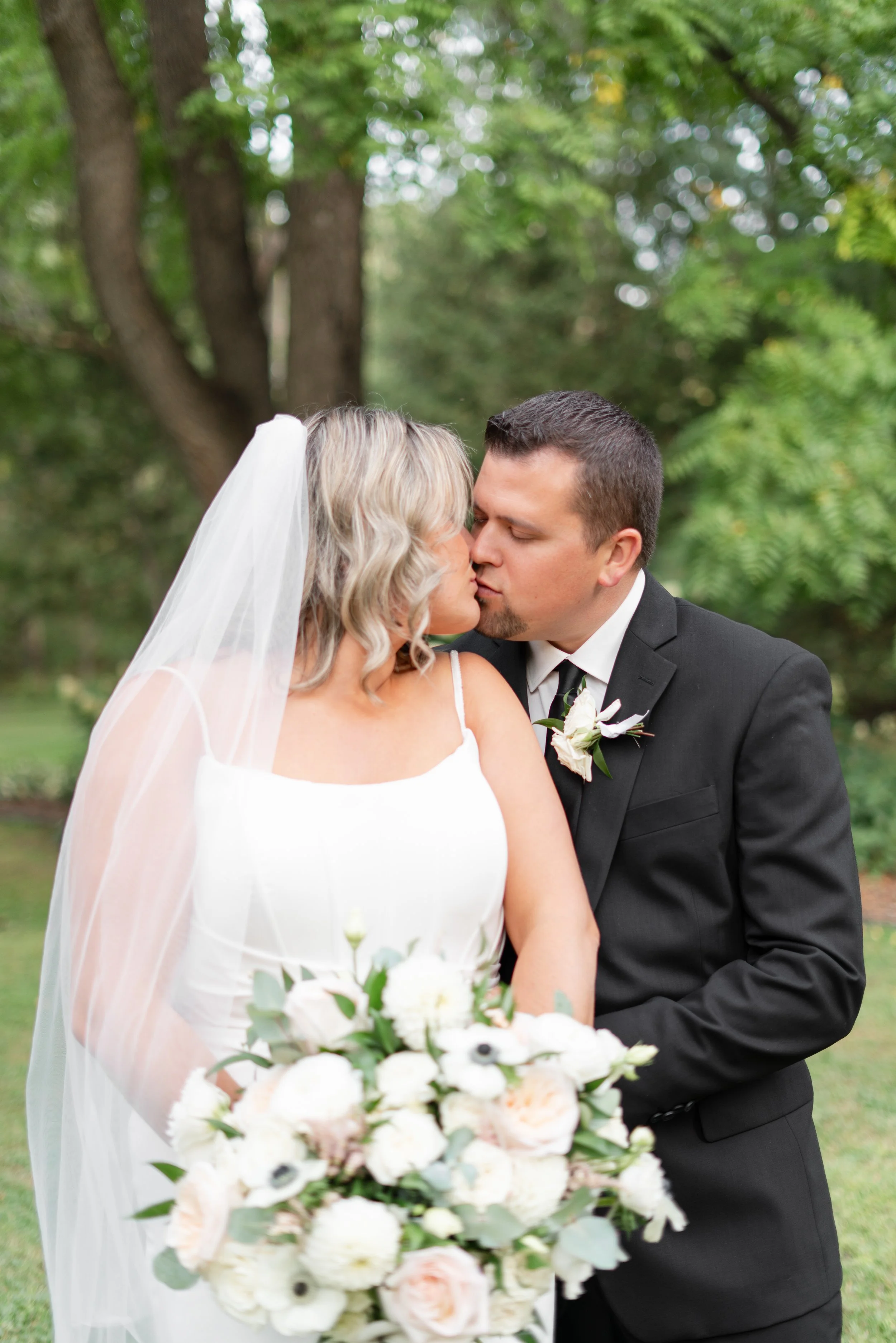 Bride and groom kissing outdoors, bride holding large white floral bouquet. Pemrboke wedding, Ontario.