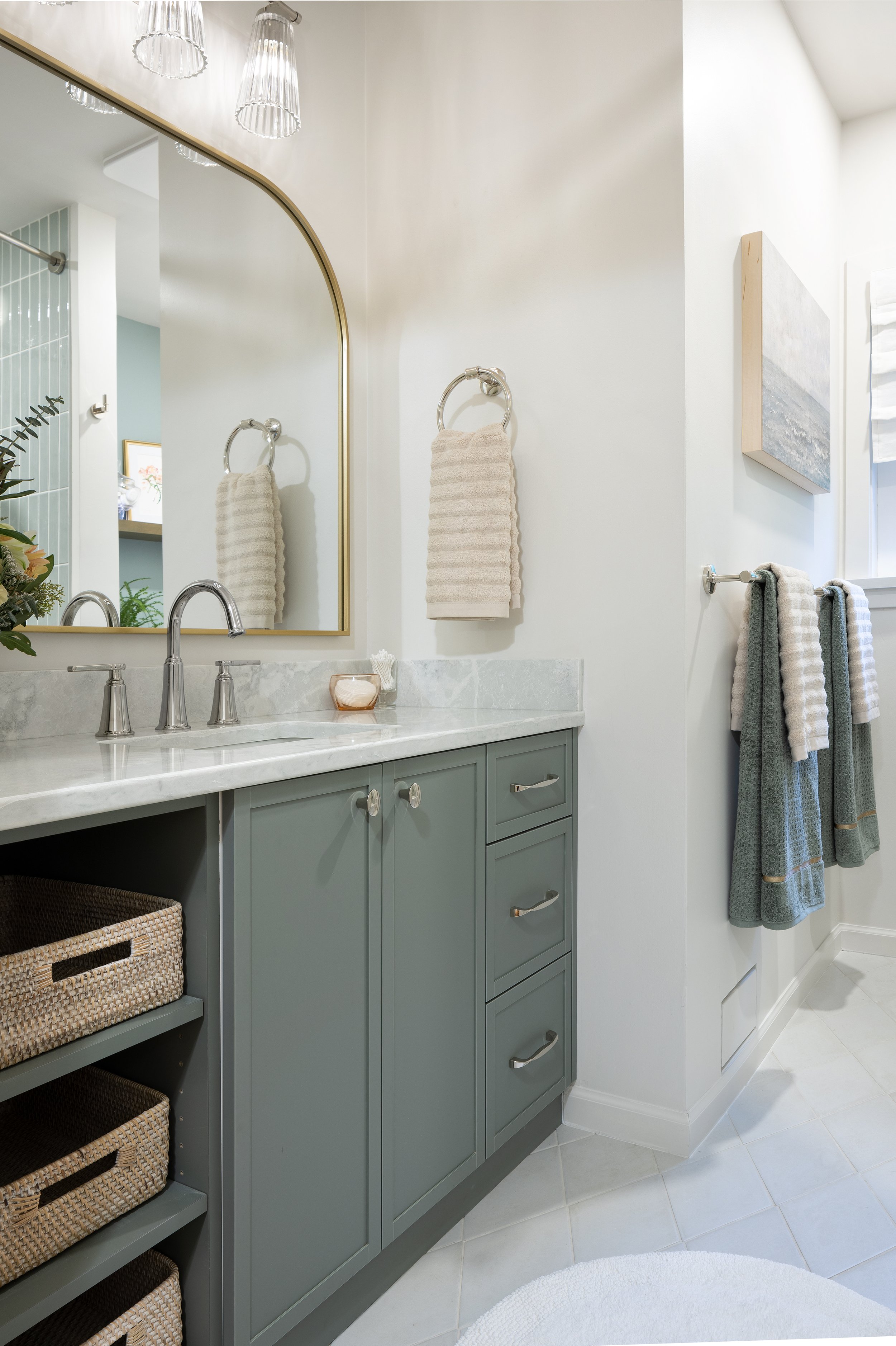 Renovated bathroom features a custom deep sage green vanity with open shelves on the left with wicker basket in lieu of traditional drawers. The center has doors and the right has three drawers. The counter is quartz and it is a beautiful bathroom.