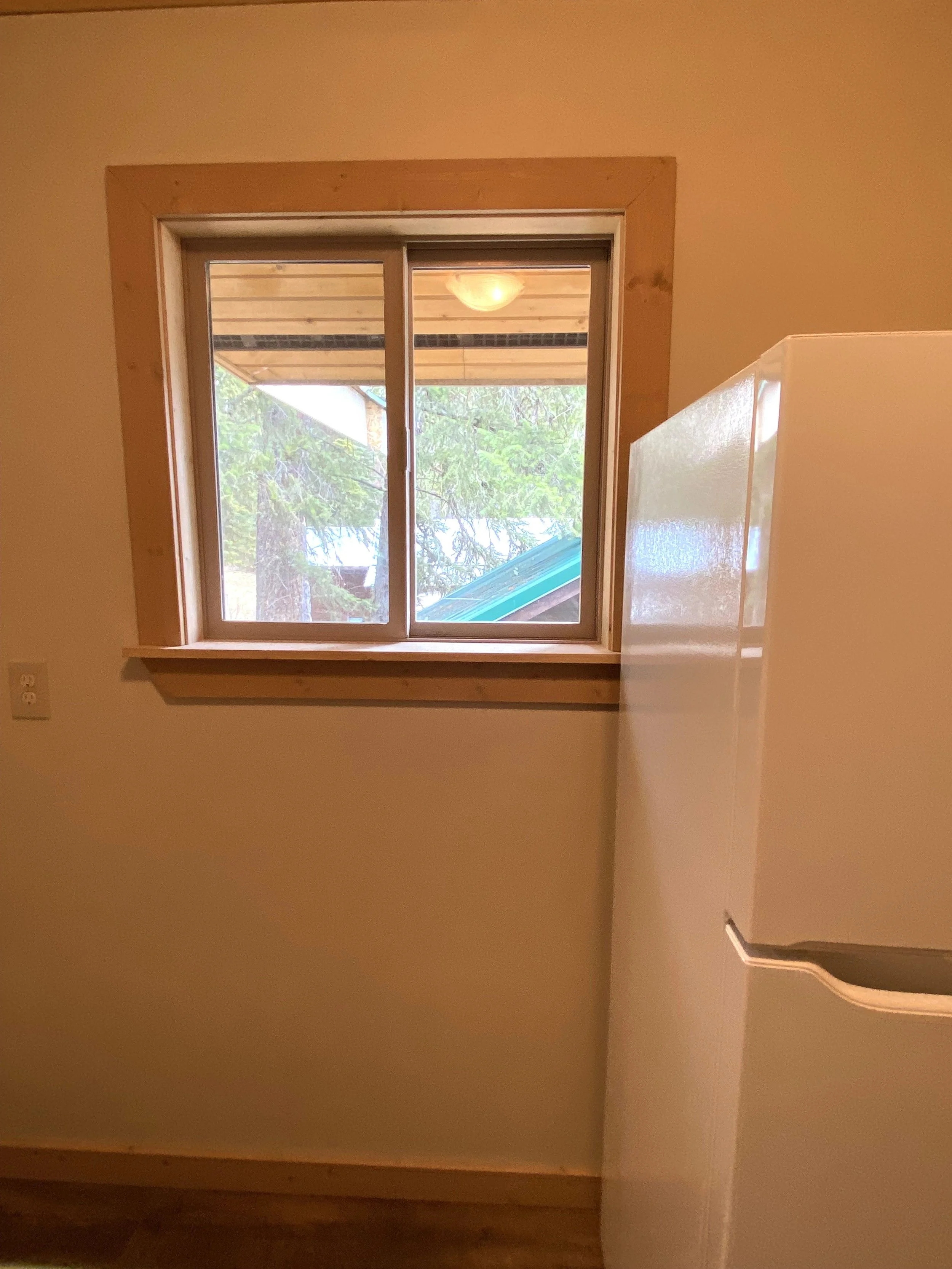 A fridge is positioned in between a wall and window but the fridge doesn't fit, it is too large, and covers the window trim. Construction error because they knew the size of fridge, but forgot about the trim install.
