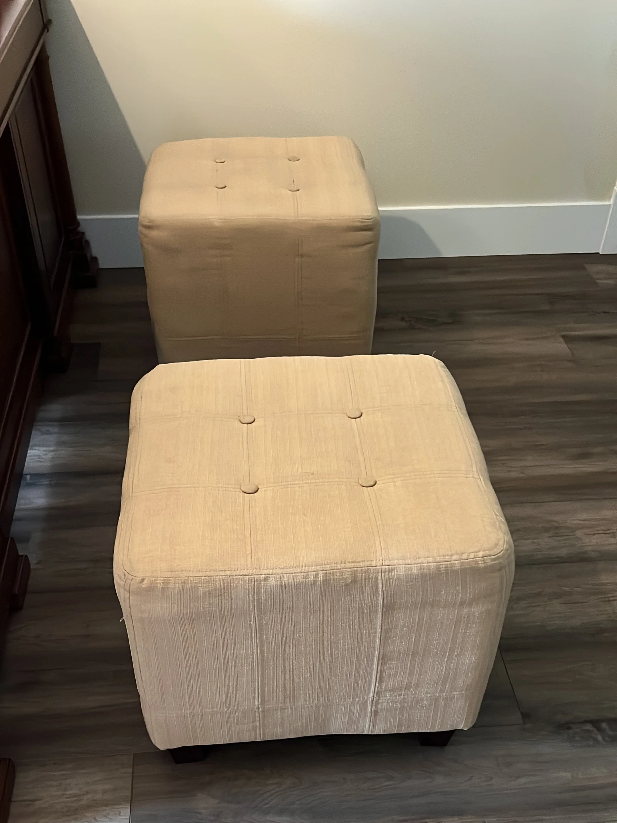 A pair of cube ottomans are slightly dated with the traditional 4 buttons on top of the seats. They look worn from a lot of use.