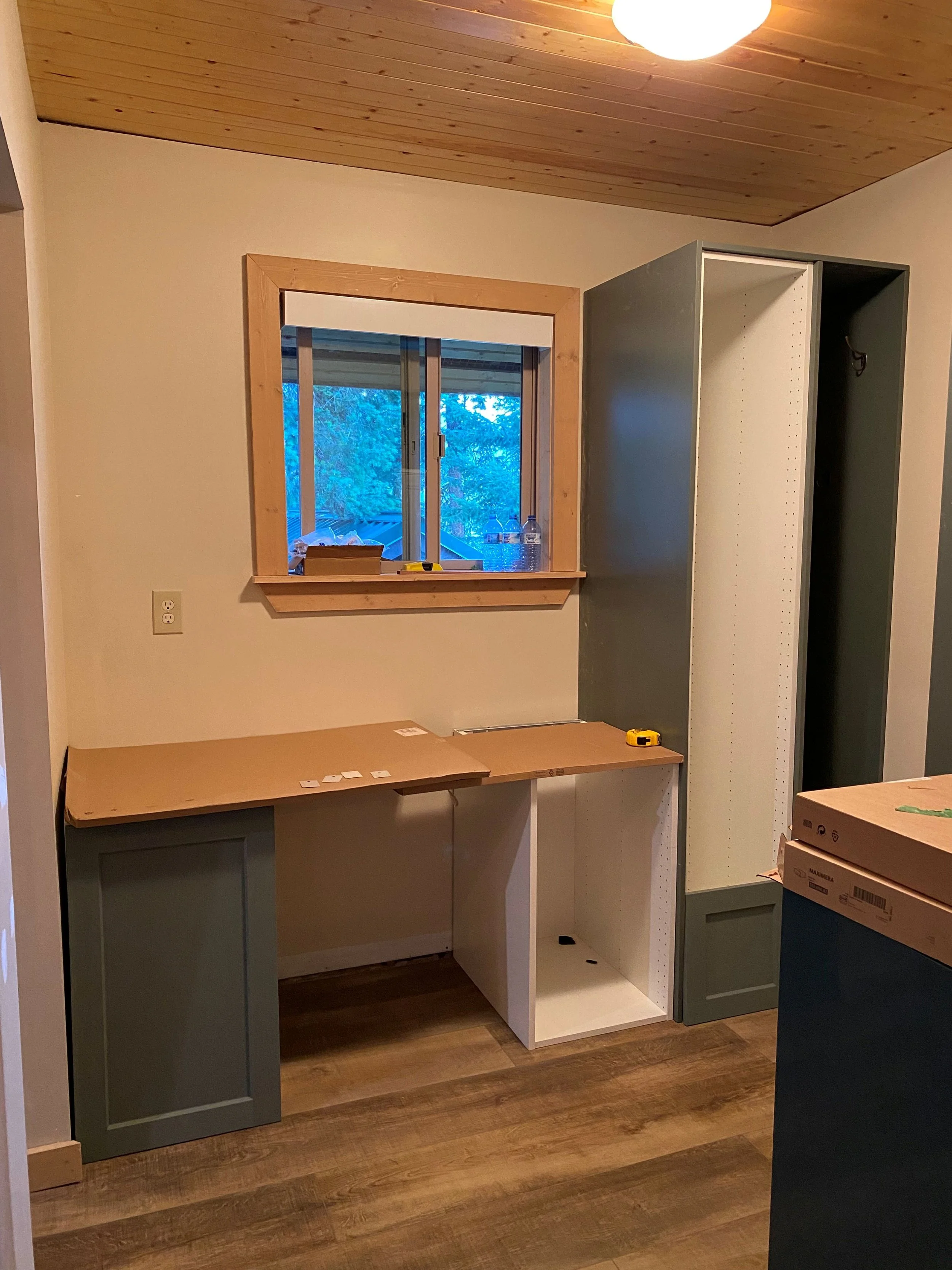 Tall IKEA kitchen cabinet with green cover panels and custom open broom cubby closet. Lower IKEA cabinets have white ENKOPING have been covered with green architectural film to blend with the green cover panels.