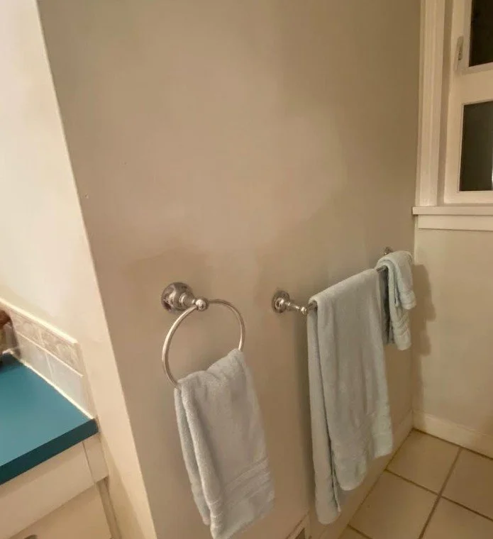 Ugly bathroom wall is pale and mottled. The towel racks are not using the space fully and there is no art above. It is dull and uninspiring.