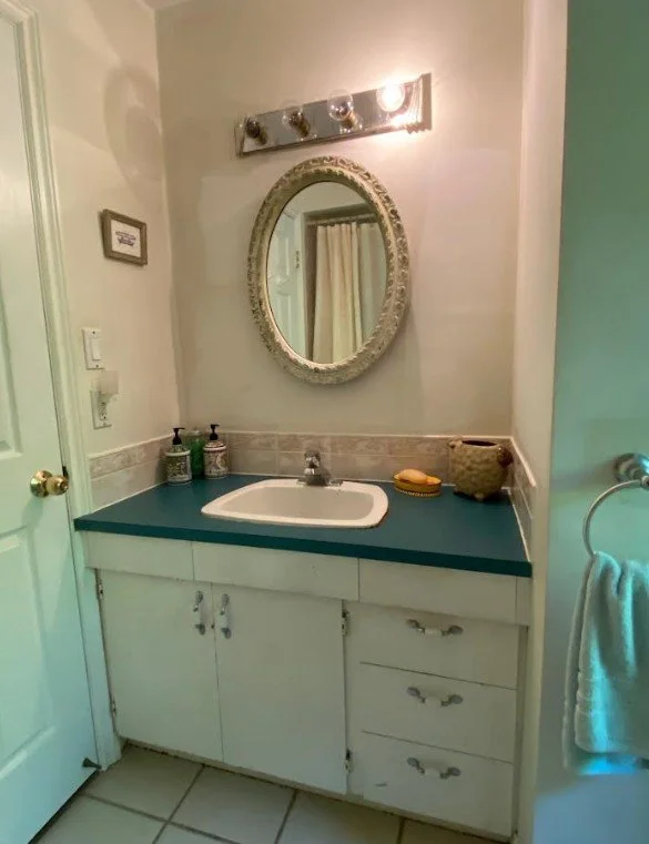 A very worn and dated bathroom vanity from the late 1950s looks ugly and worn. The backsplash is from the 1990s and is dated. The vanity mirror above is small on the wall and the vanity light above the mirror only has one light out of four working.