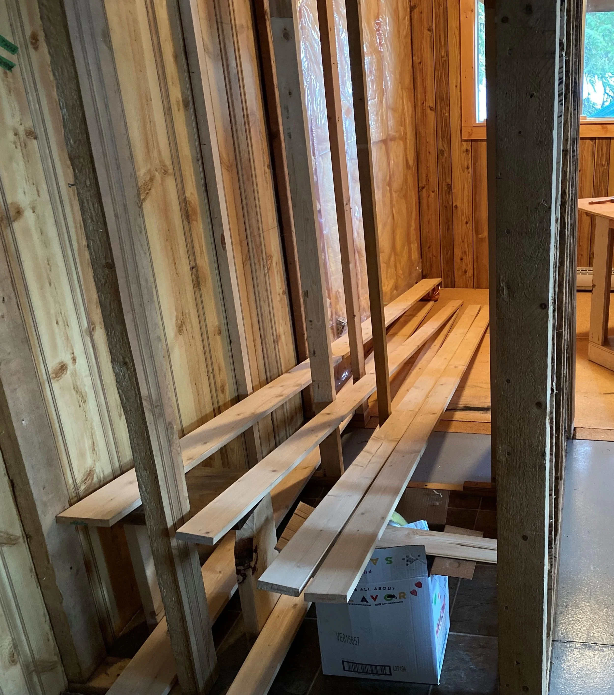 Closet studs are in view. Wall material has been removed in this cabin renovation, so the room beyond is visible. Overall it is a small closet with 9 2x4's standing up.