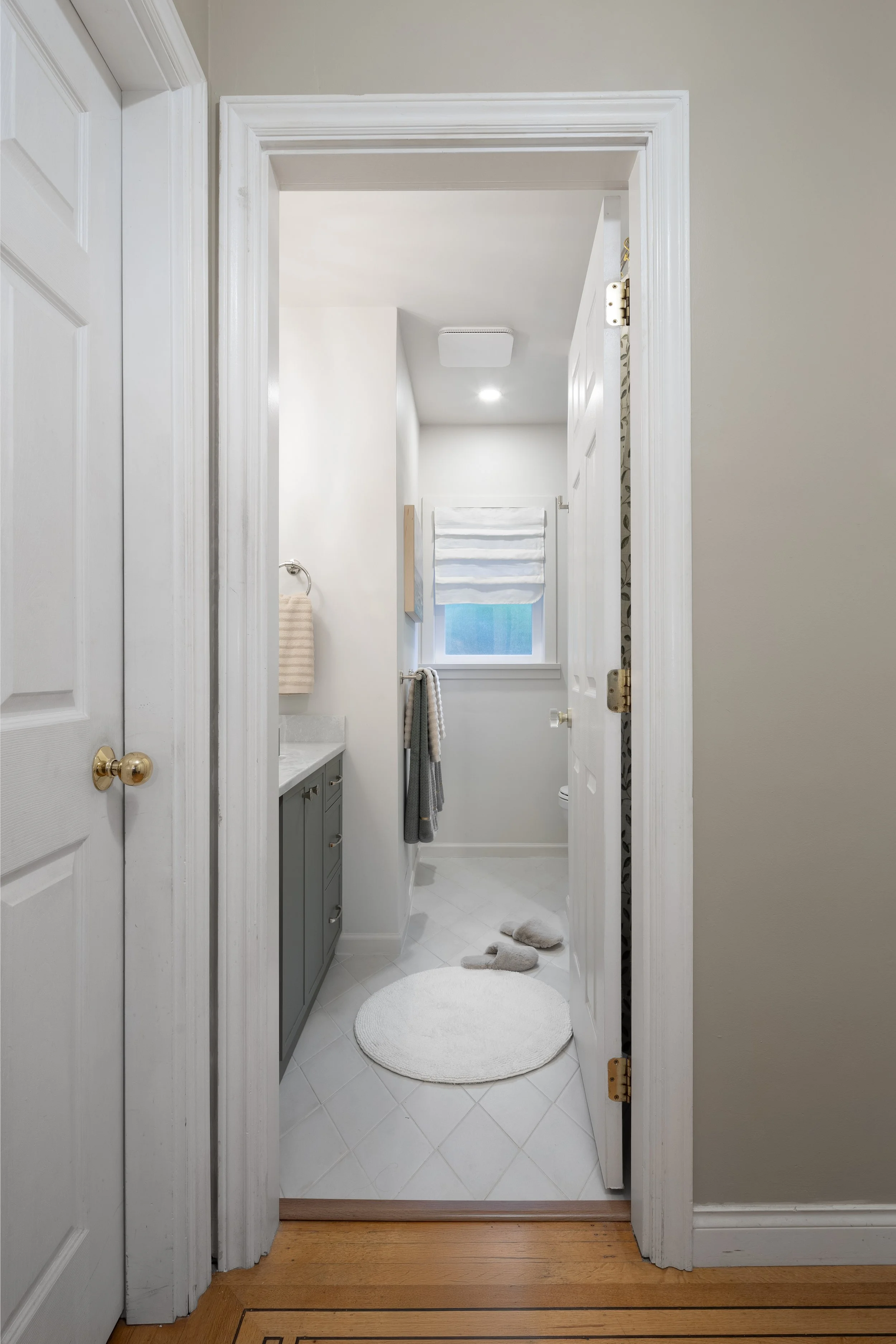 After image of a late 1950s bathroom renovated in a bungalow house in North Vancouver, BC. The new bathroom entry reveals new recessed ceiling light, a new fan to help with moisture in a bathroom and overall it is a warm white and soft green vanity.