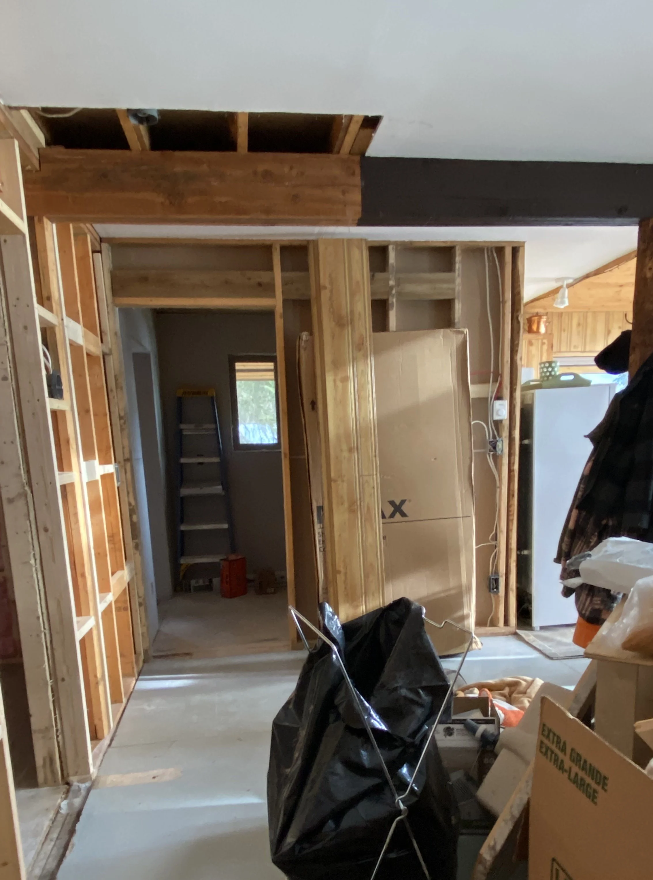 Cabin renovation is underway and the space is starting to take shape with a closet removed and a new doorway installed. A beam above is half unfinished wood and the other half is painted brown, indicating where the closet was and where it stopped.