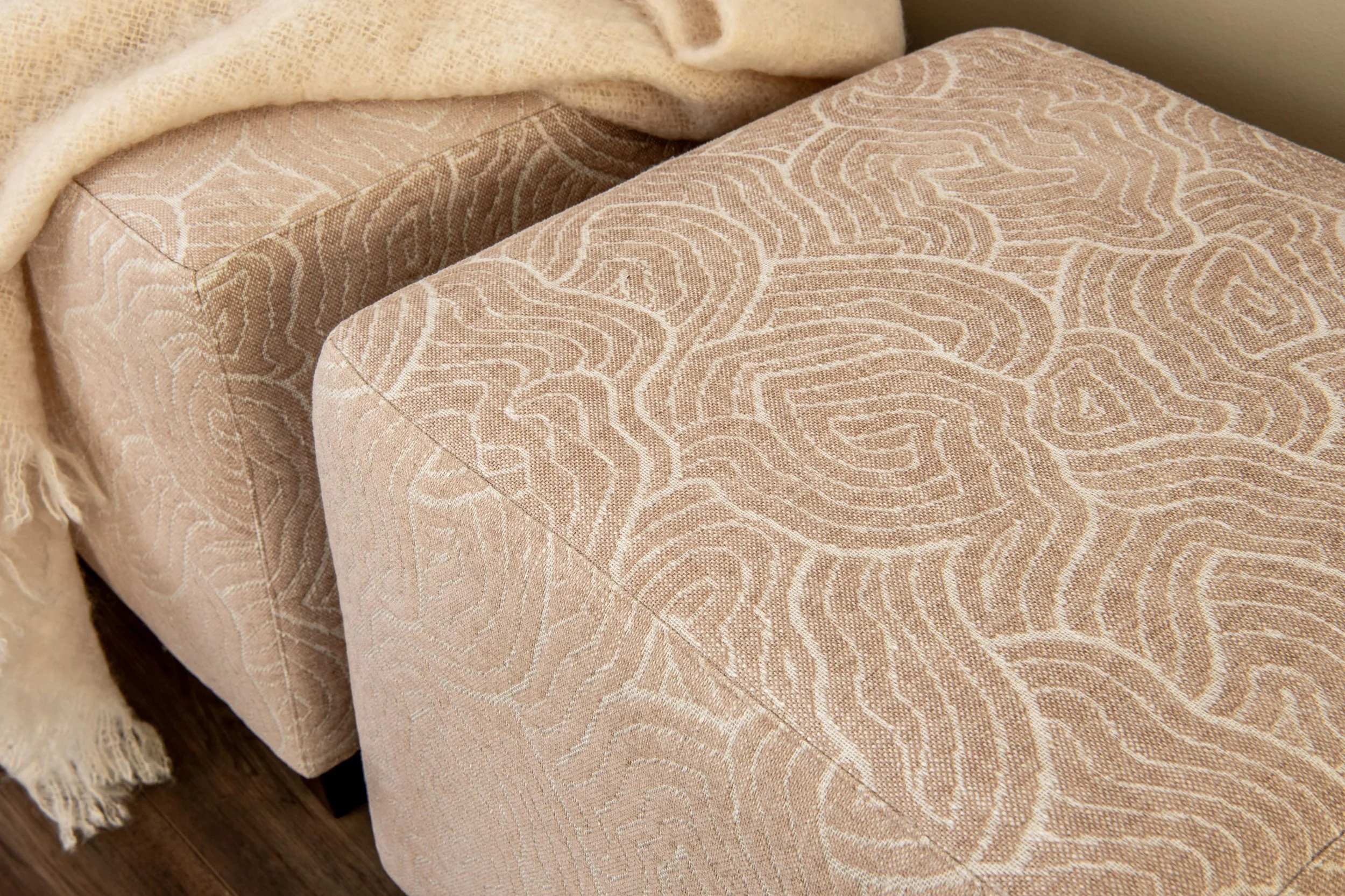 A pair of square cube ottomans have been reupholstered in Tonic Living's "Quince" in Petal Pink Colorway. They pattern is modern swirly like clouds.
