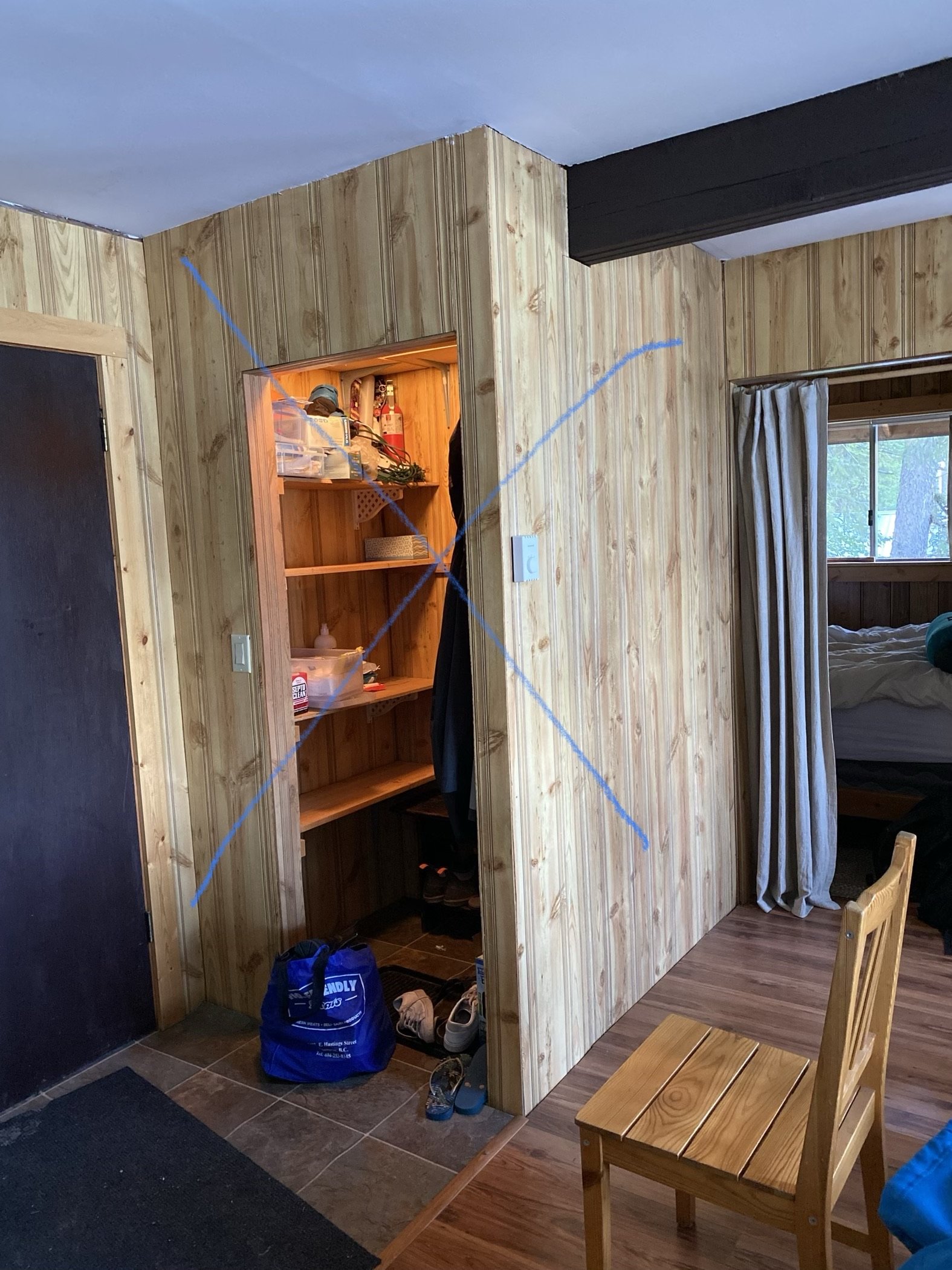 A "before" photo of a closet wall that has an X on the photo, indicating this closet and wall is going to be removed in an upcoming renovation.
