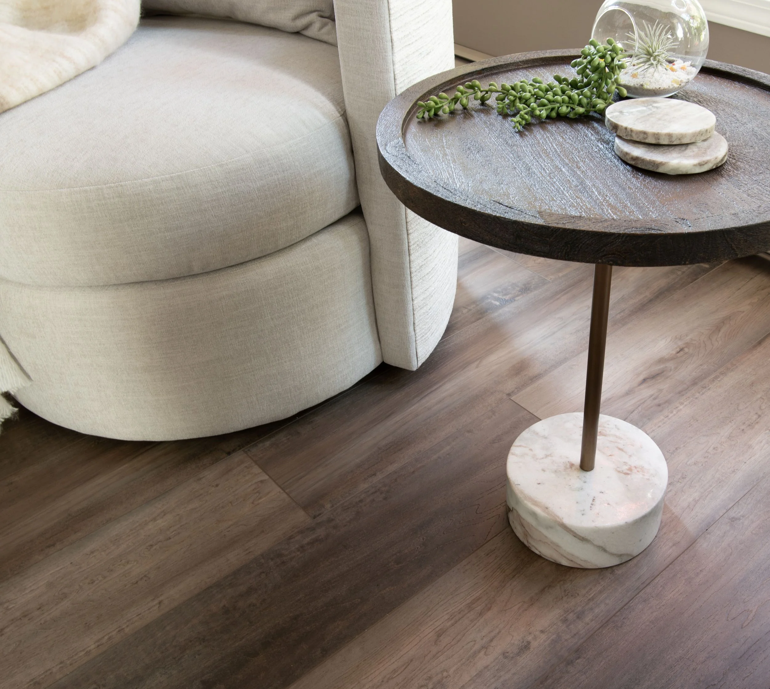 Van Gogh Olive Swivel Chair in light grey alongside a small side table from Renwil. Brown wood top about 18" diameter, gold metal stand into a round marble base to hold it up.