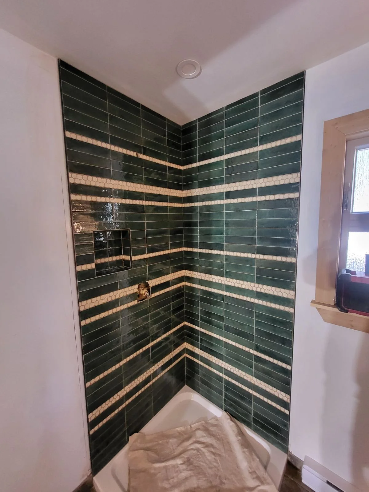 Green lume 2" x 9" Ames Tile is stacked vertically in a corner shower. Small white hex is included to create stripes at different heights throughout. This helps break up the dark green color and give the solid green some visual interest.