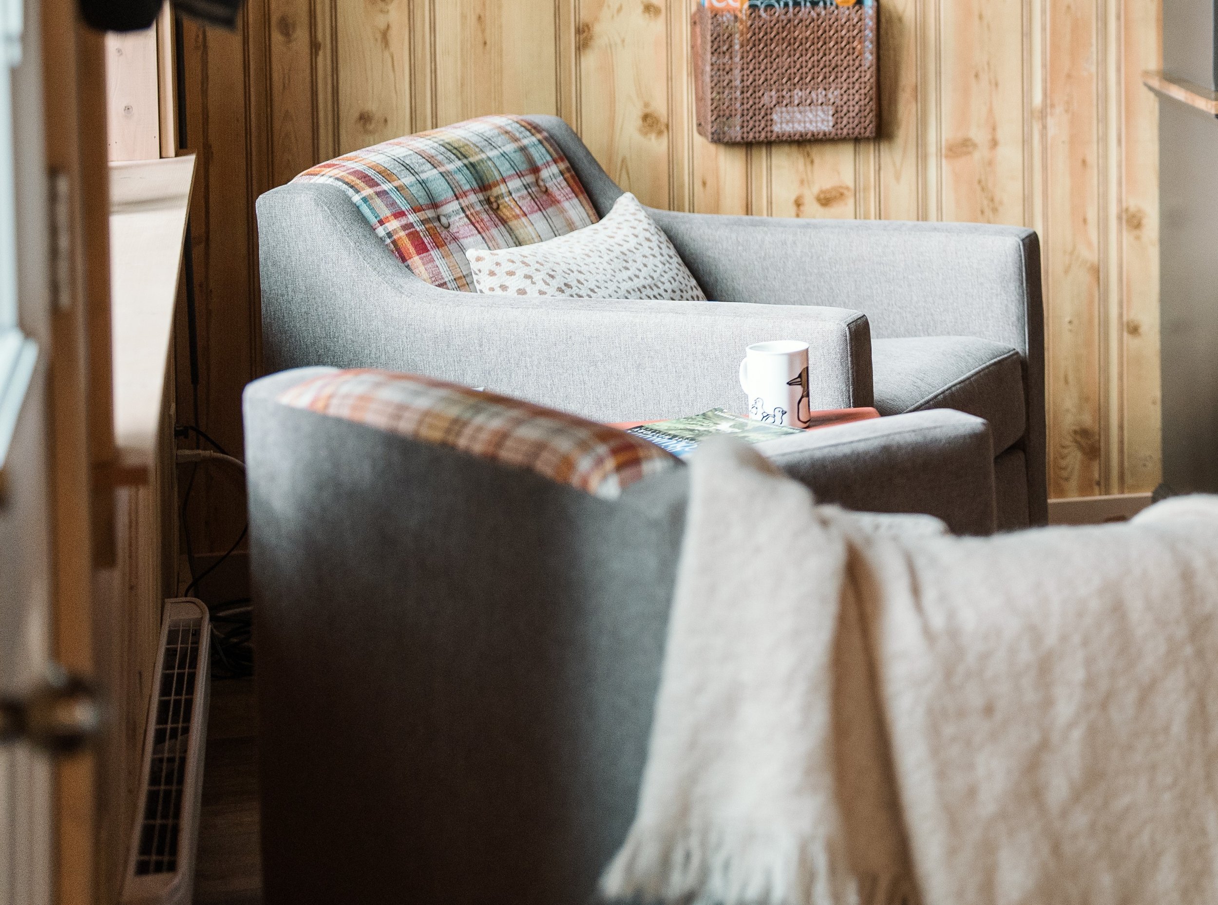 A pair of swivel chairs are mostly in a soft grey-beige color but the inside backs are upholstered in a separate vibrant plaid fabric with colors of red, burnt orange, golden yellow, turquoise, white, grey, brown.
