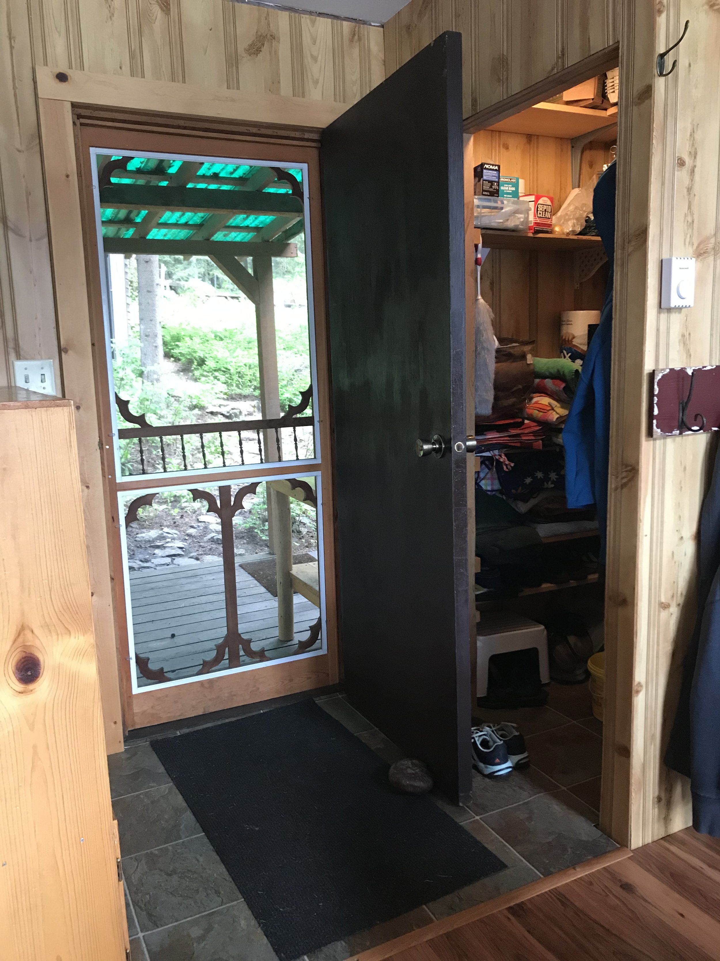 A classic cabin screened door is closed and keeps the bugs out. The main door is open allowing the screen door to allow to help with the breeze. A hard to access closet is behind the open door, making it difficult to access.