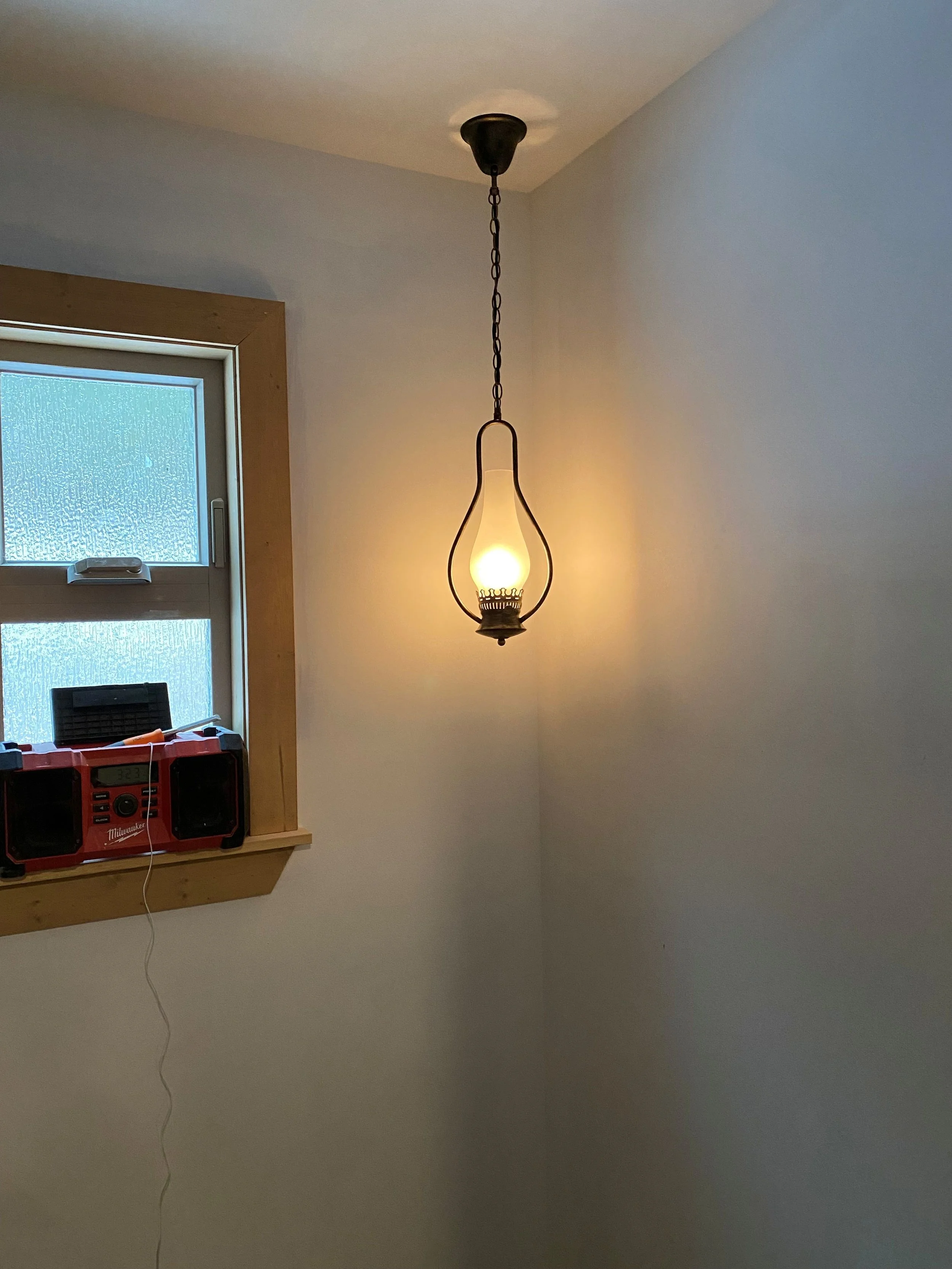 Before photo of the corner of a bathroom that has one window and one pendant light. The oil rubbed bronze antique oil lantern pendant hangs in the corner. The walls are unfinished with white primer only. Getting ready to add some color to this room.