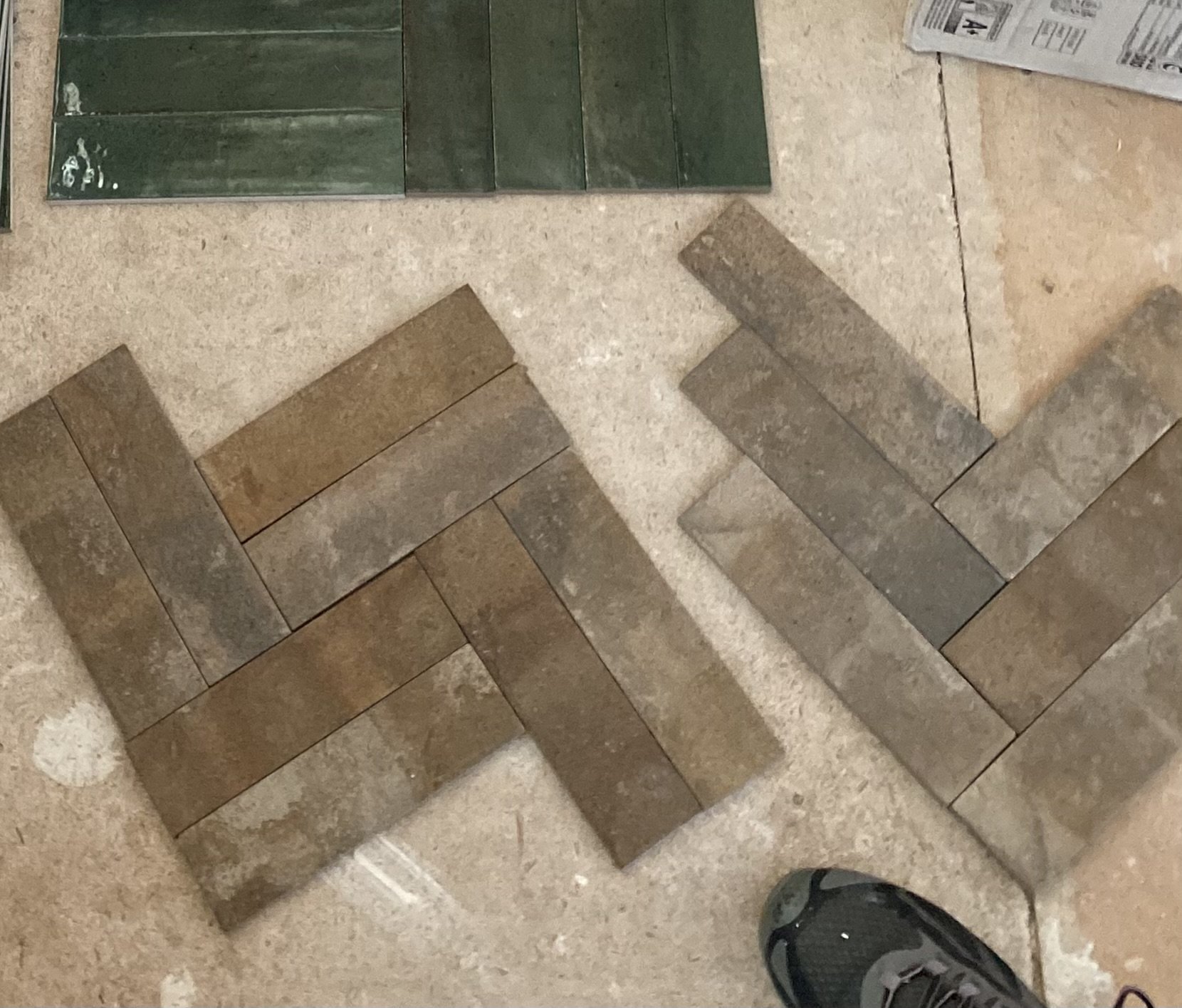 Rustic brown and grey brick porcelain tile sits on the ground in two different patterns. One is in the double herringbone pattern and the other is a traditional single herringbone pattern.