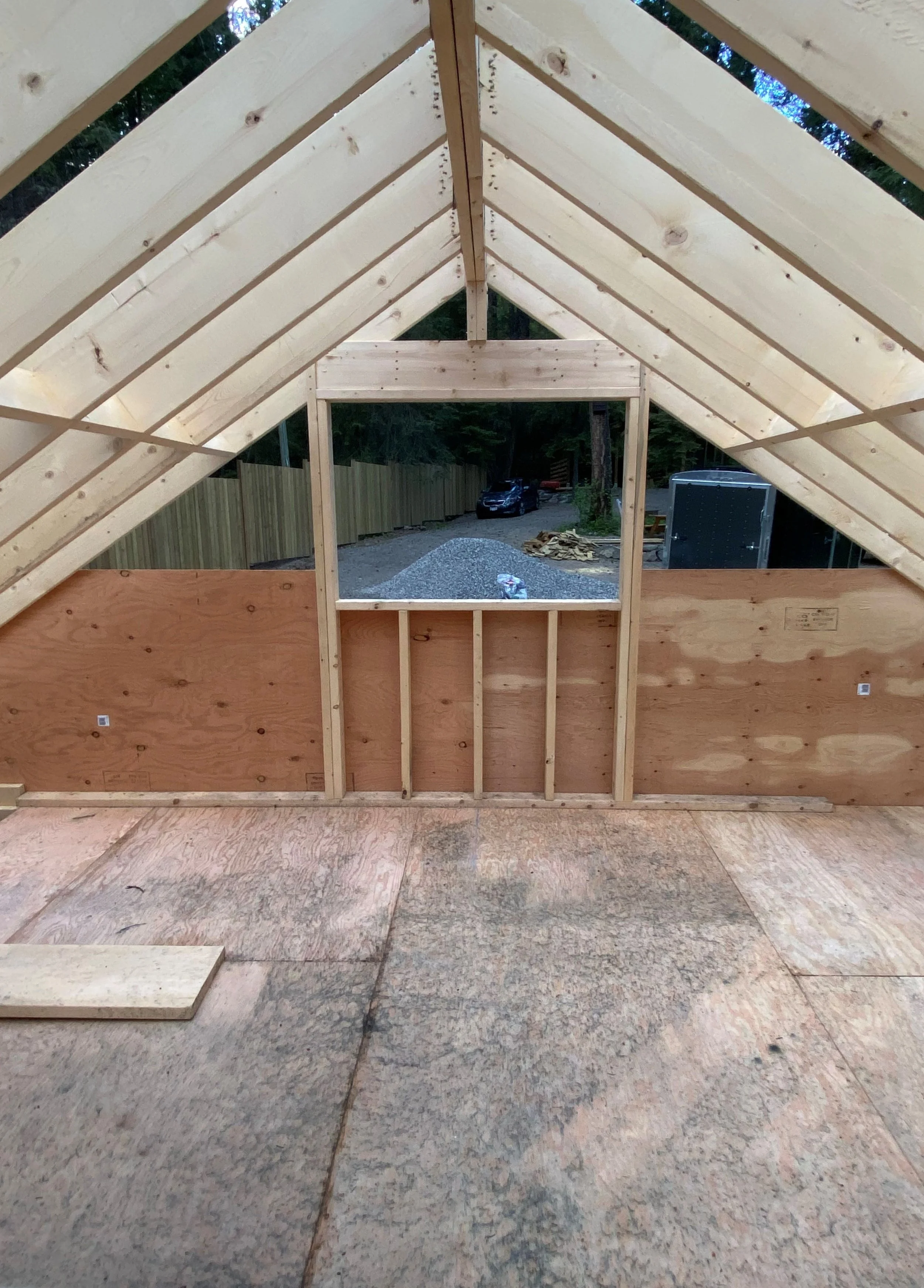 Framing of a angled peaked roof attic bedroom with one window. Plywood floor and two by six construction materials are used.