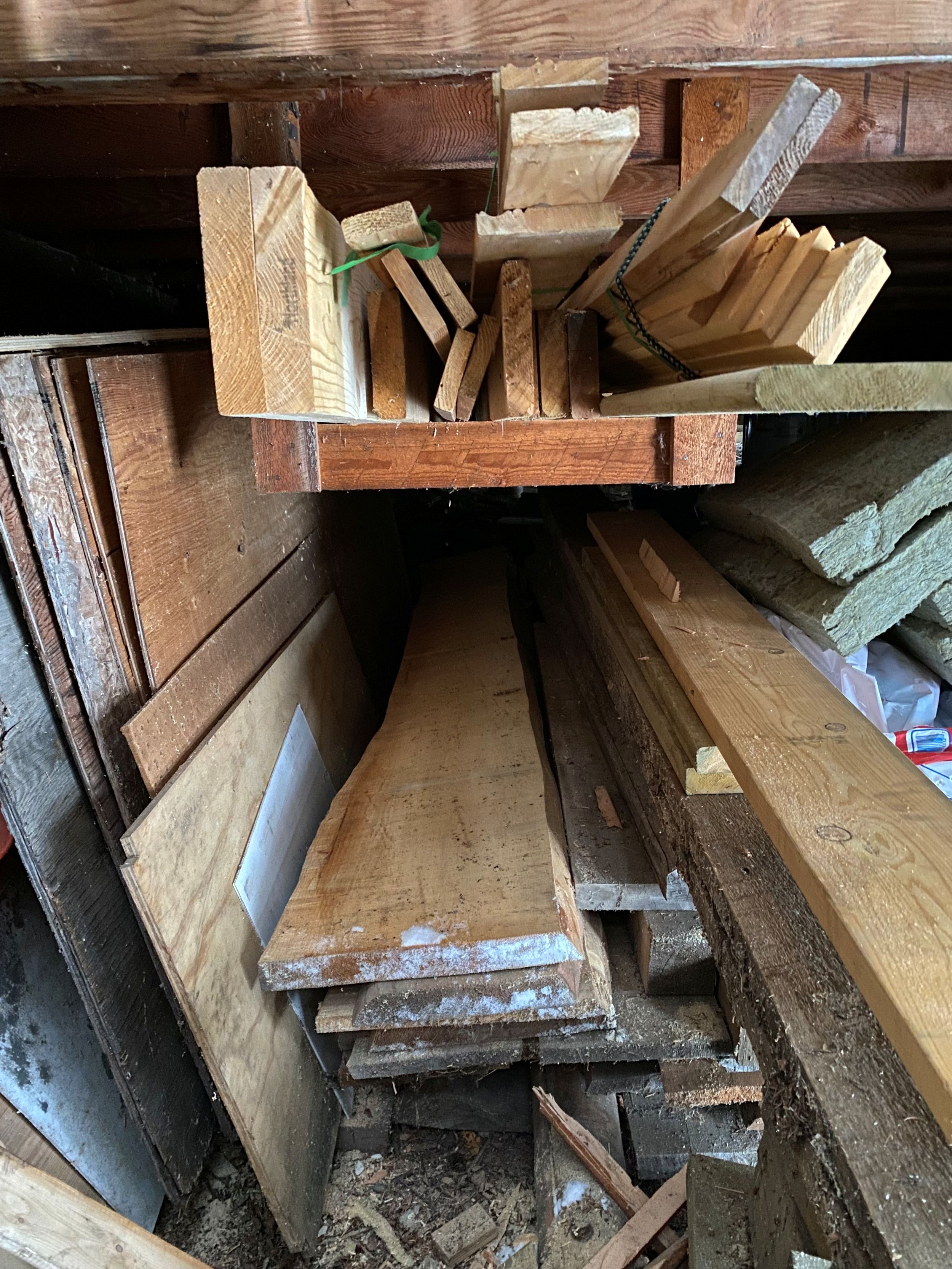 A pile of wood of varying shapes and sizes are found under a cabin, kept dry from the elements. Raw live edge cuts are possible contenders to use as a table top. Species is fir and pine.