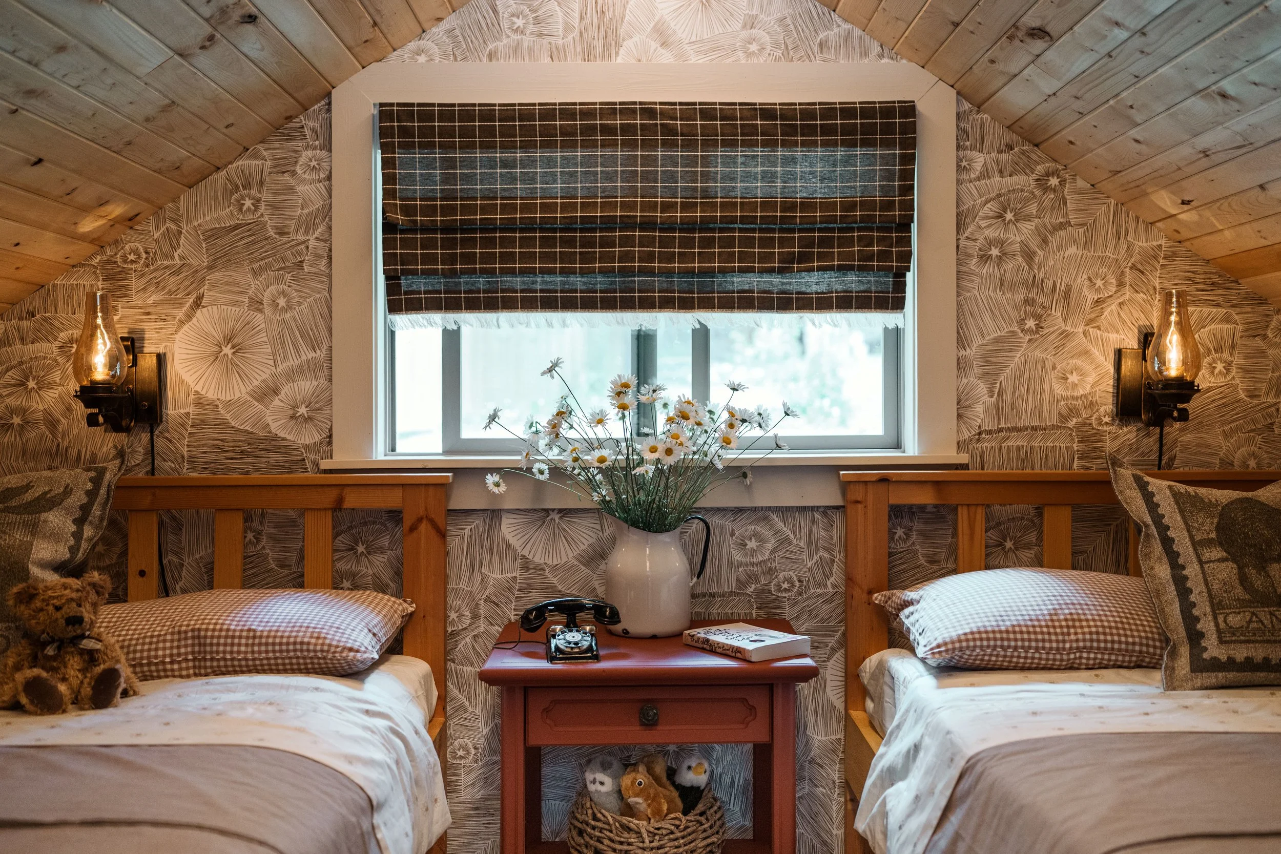 Kid friendly bedroom in a loft in a cabin. Pine ceiling and headboard accents. Rustic red side table and modern star wallpaper make this a cute and cozy bedroom.