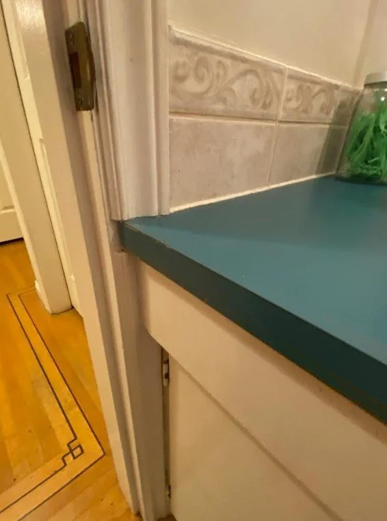 A bathroom vanity counter is too large to fit into the area for the vanity, and so the doorframe has been cut for the counter to slide into it. It looks ridiculous. DIY renovation gone bad.