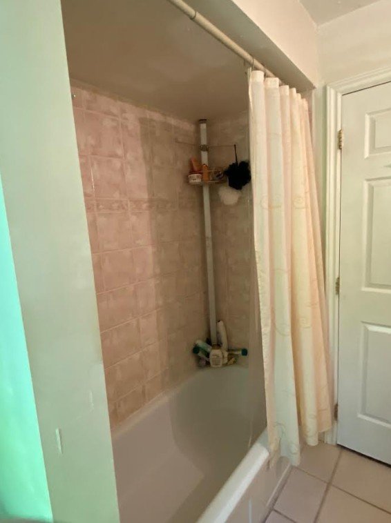 Before image of a dated and plain bathtub and shower area in a late 1950s home. Plain beige and cream colors make it look depressing and uninviting. The ceiling is lowered and makes it feel small.