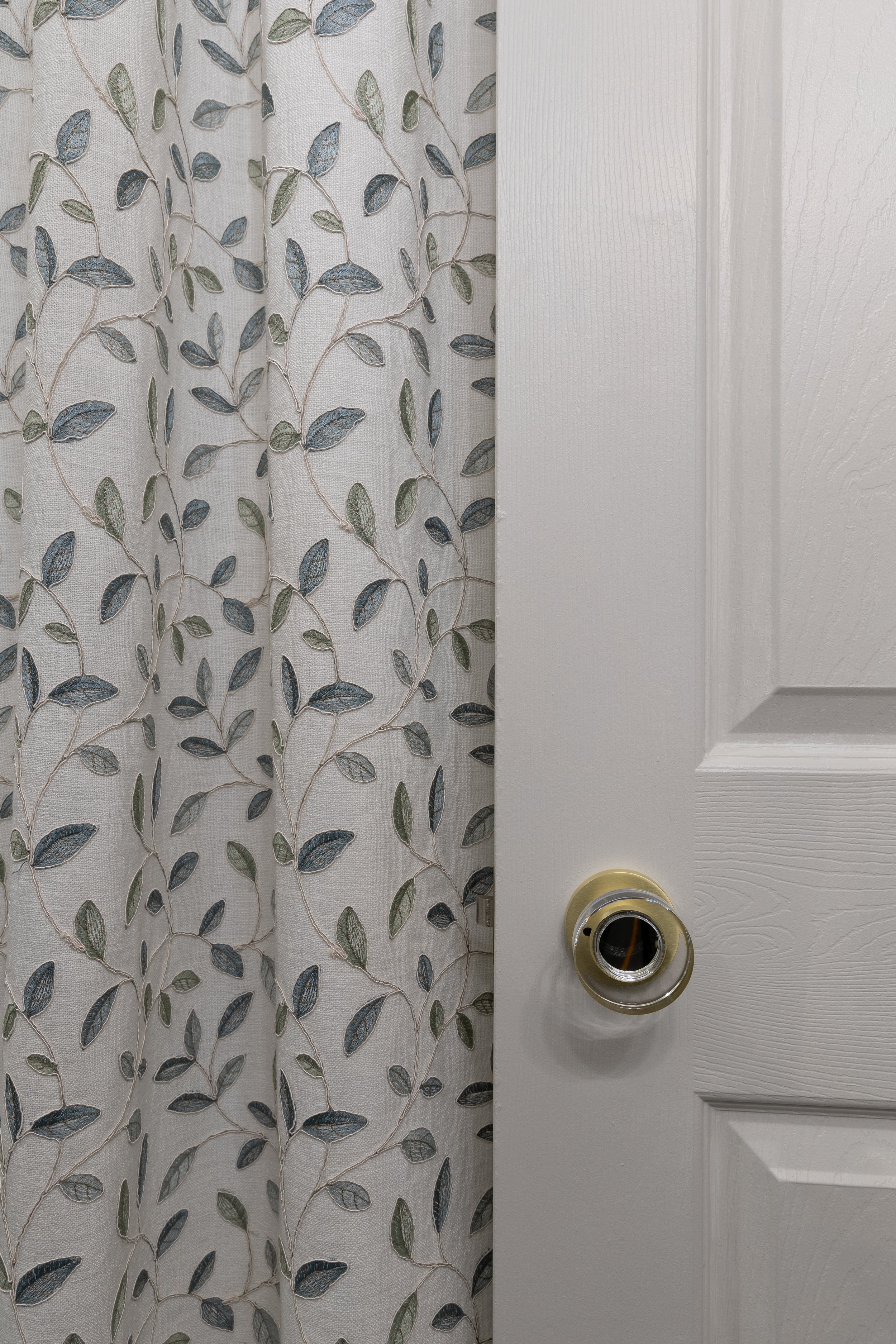 Covington Ivy Embroidered Drapery Fabric in Silver Sage and a white door with a new Explore Hardware Seychelles Gold and Crystal round privacy door hardware