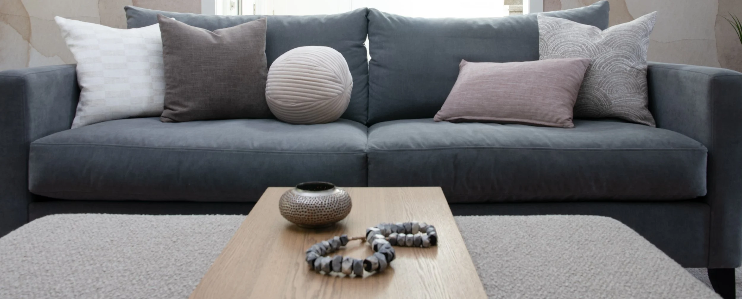 New sofa from Van Gogh: Sooke model in blue-grey Breton Storm. Five toss cushions in random size, color and patterns enliven the solid sofa color. Style In Form Forest Ottoman in Truffle Boucle greige color with white oak sliding table.