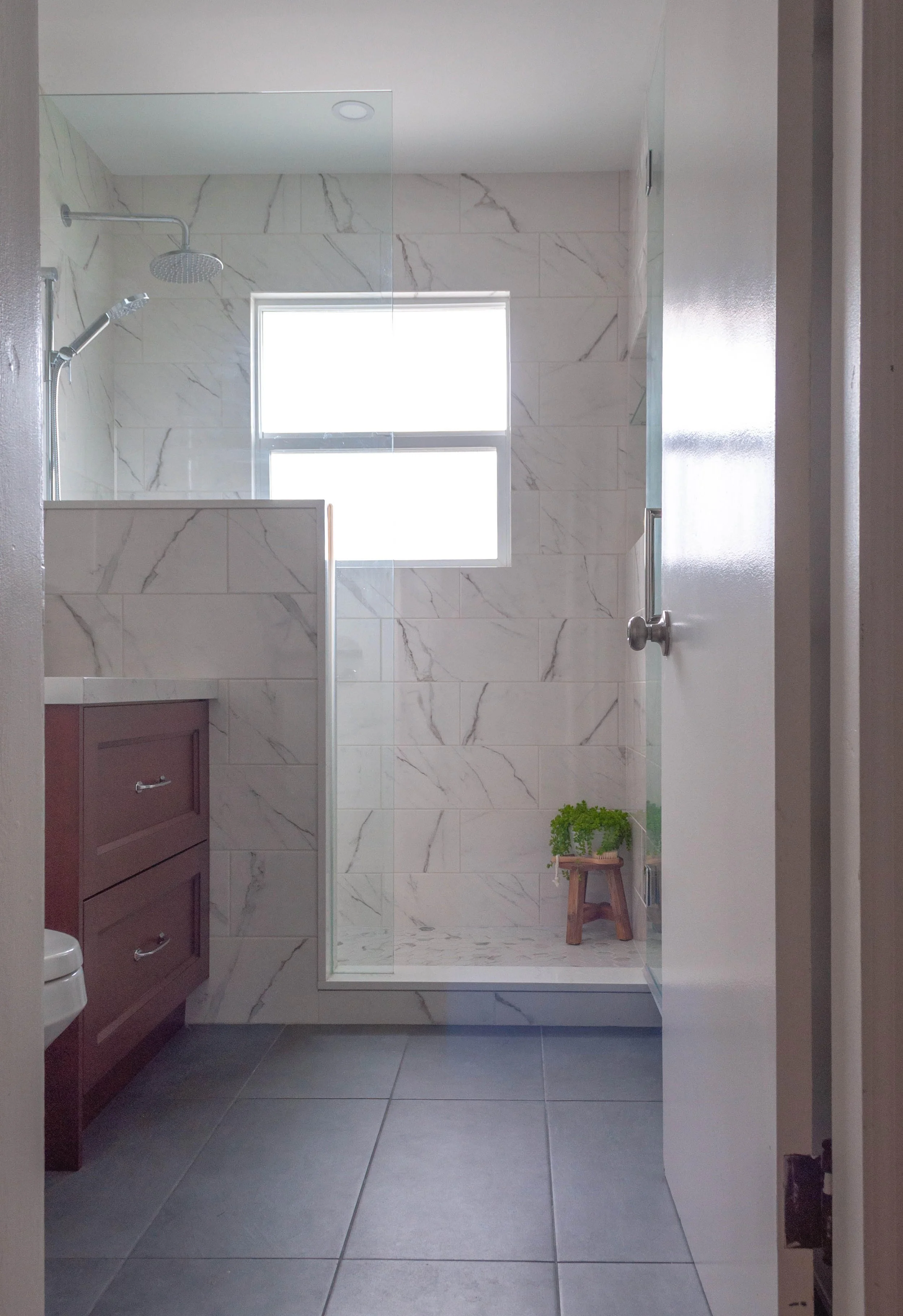 Cool, contemporary faux marble tile walk-in-shower with a window in the shower.