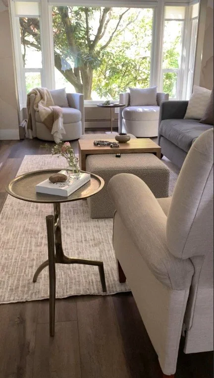 A soft colored, neutral but not boring, living room update. Up close is a metal gold side table with a weathered patina and branch like legs which are reminiscent of the branches viewed directly across the room, outside in the garden.