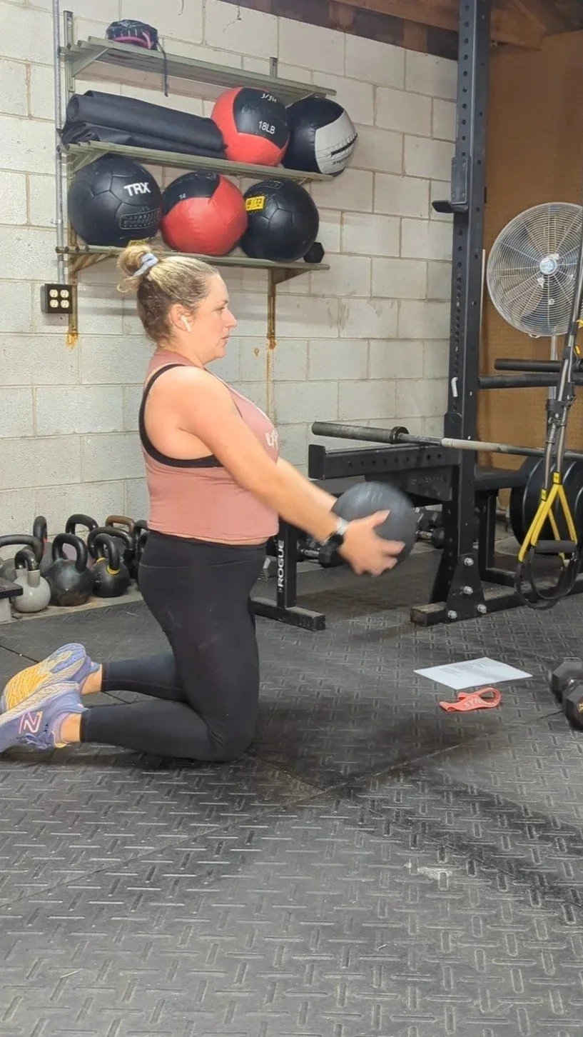 Strong woman in her 40s working out with a slam ball while kneeling.
