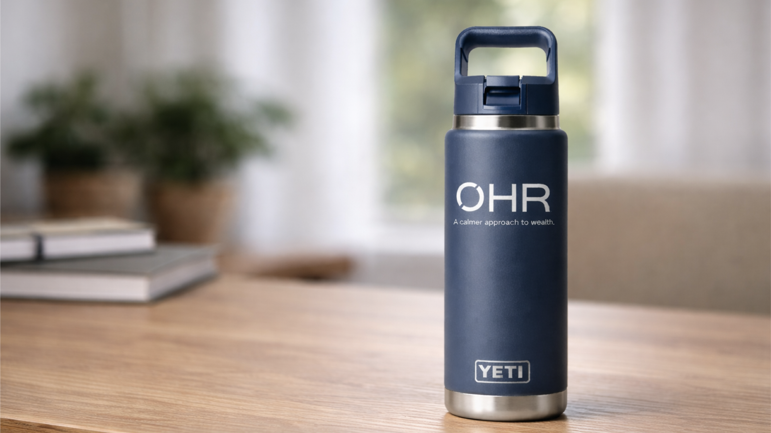 A navy blue YETI water bottle on a wooden table, with a blurred background of plants and books, and the label 'OHR' with the slogan 'A calmer approach to wealth.'.