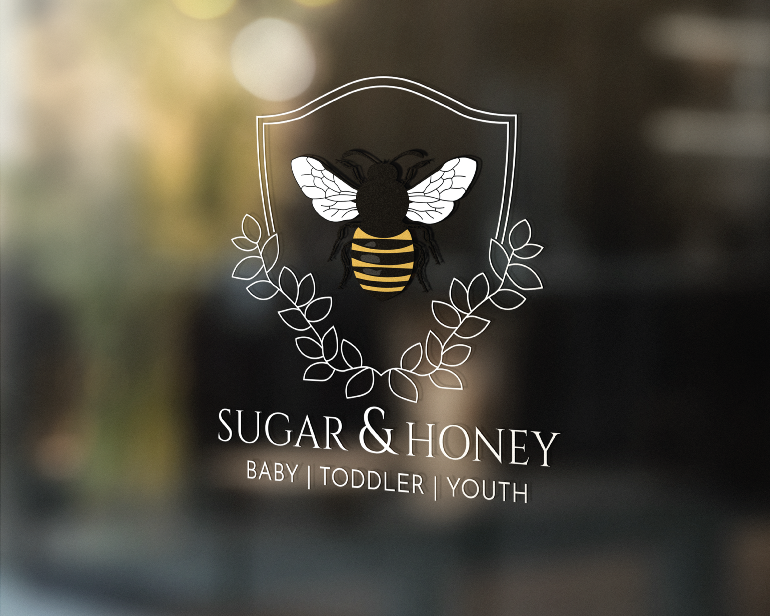 Logo for Sugar & Honey featuring a bee with white wings and a yellow and black striped body, surrounded by a laurel wreath, with text indicating it is for baby, toddler, and youth products.