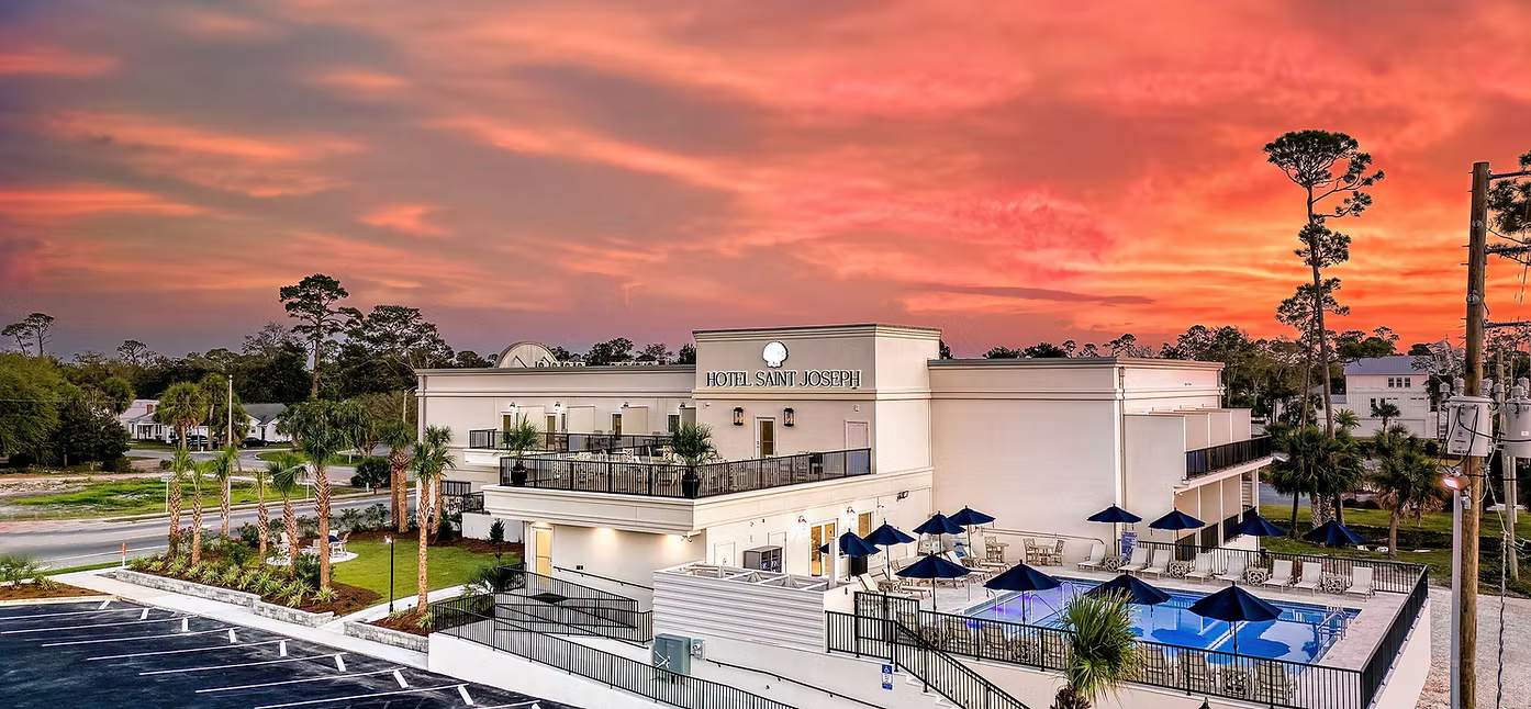 Exterior view of Hotel Saint Joseph during sunset with a pool area, outdoor seating, and palm trees.