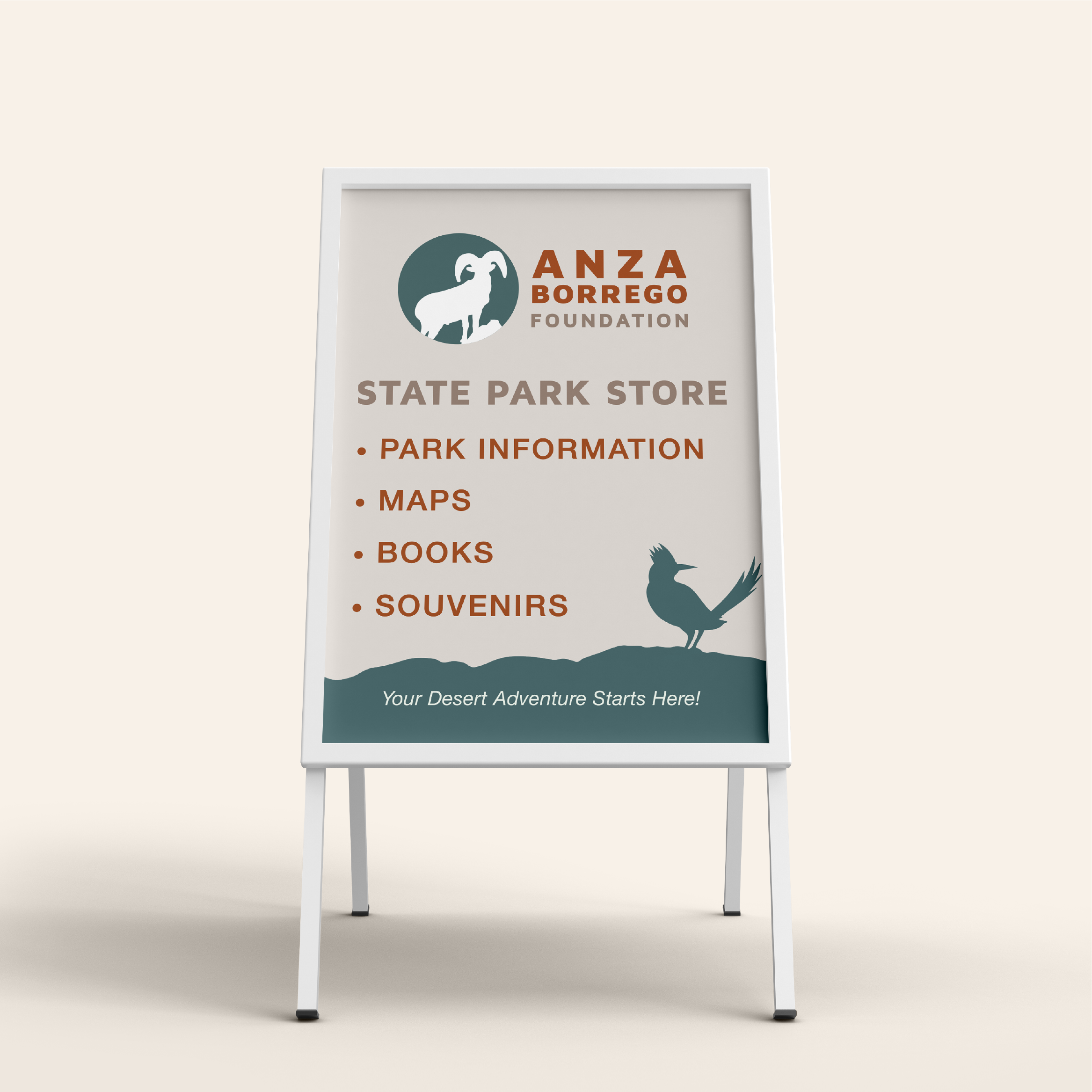 A white A-frame signboard for the ANZA Borrego Foundation's State Park Store featuring park information, maps, books, and souvenirs. The sign has a logo of a ram and a bird silhouette with the slogan "Your Desert Adventure Starts Here!"