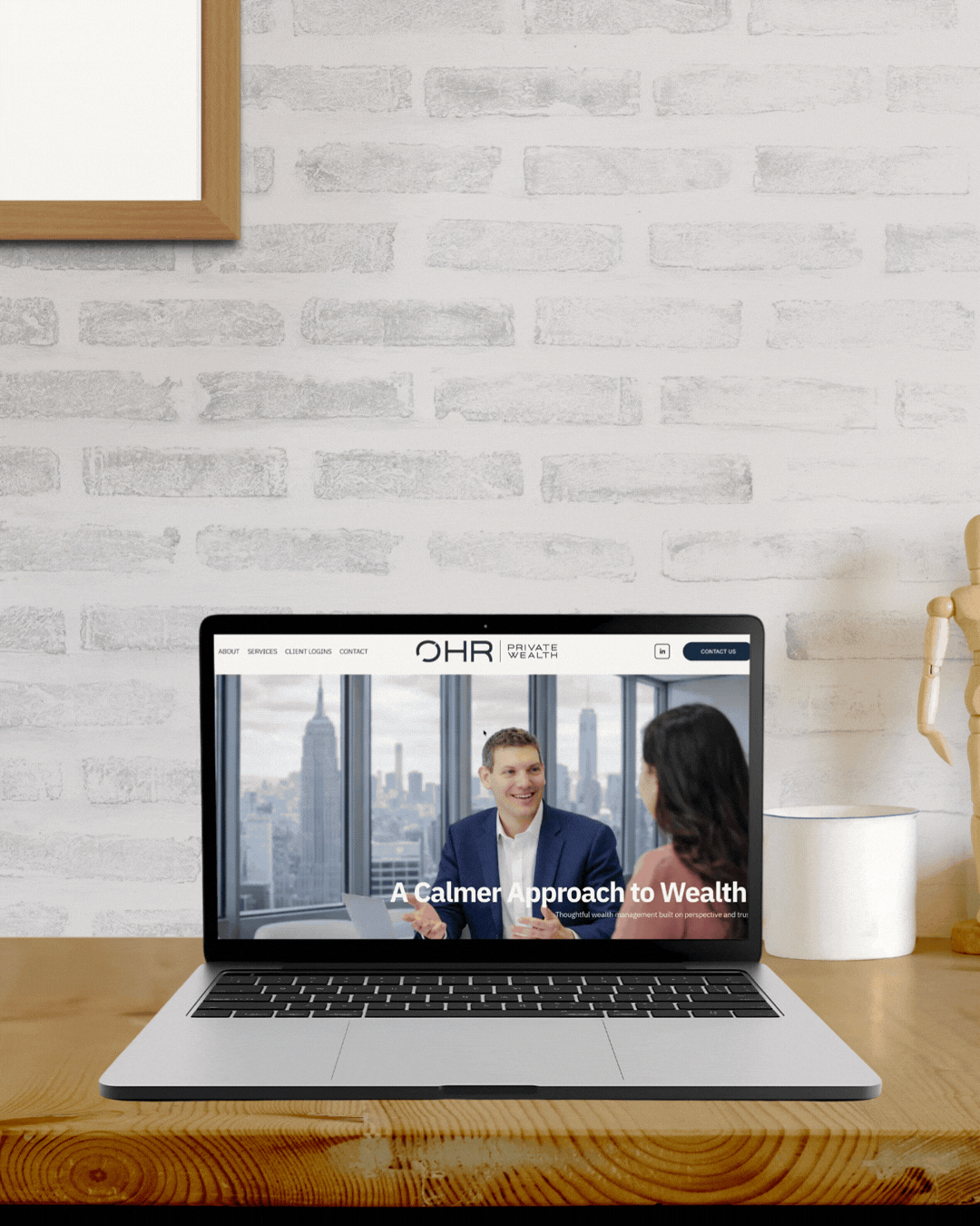 Laptop on a wooden desk displaying a website for OHR Private Wealth, showing two people in a meeting with city skyline view in the background.