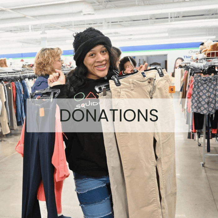 Woman holding up a pair of khaki pants at a Alabama Goodwill store with donations in the background.