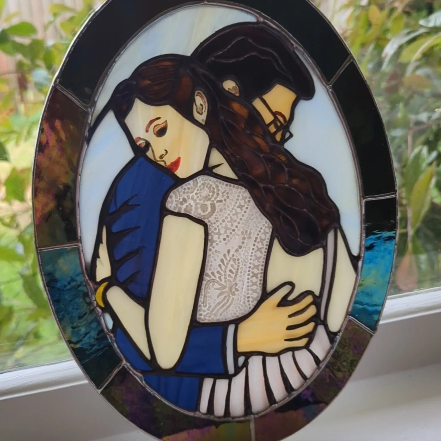 Stained glass window depicting a woman with long brown hair, wearing a blue top, holding a white mug with lace detailing. She has red lipstick and is looking down at her mug.