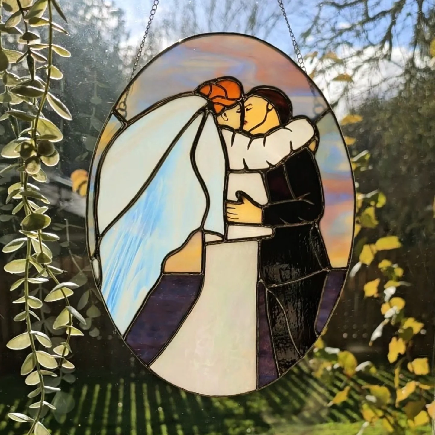 Stained glass artwork depicting a couple embracing, with a sunset and sky in the background.