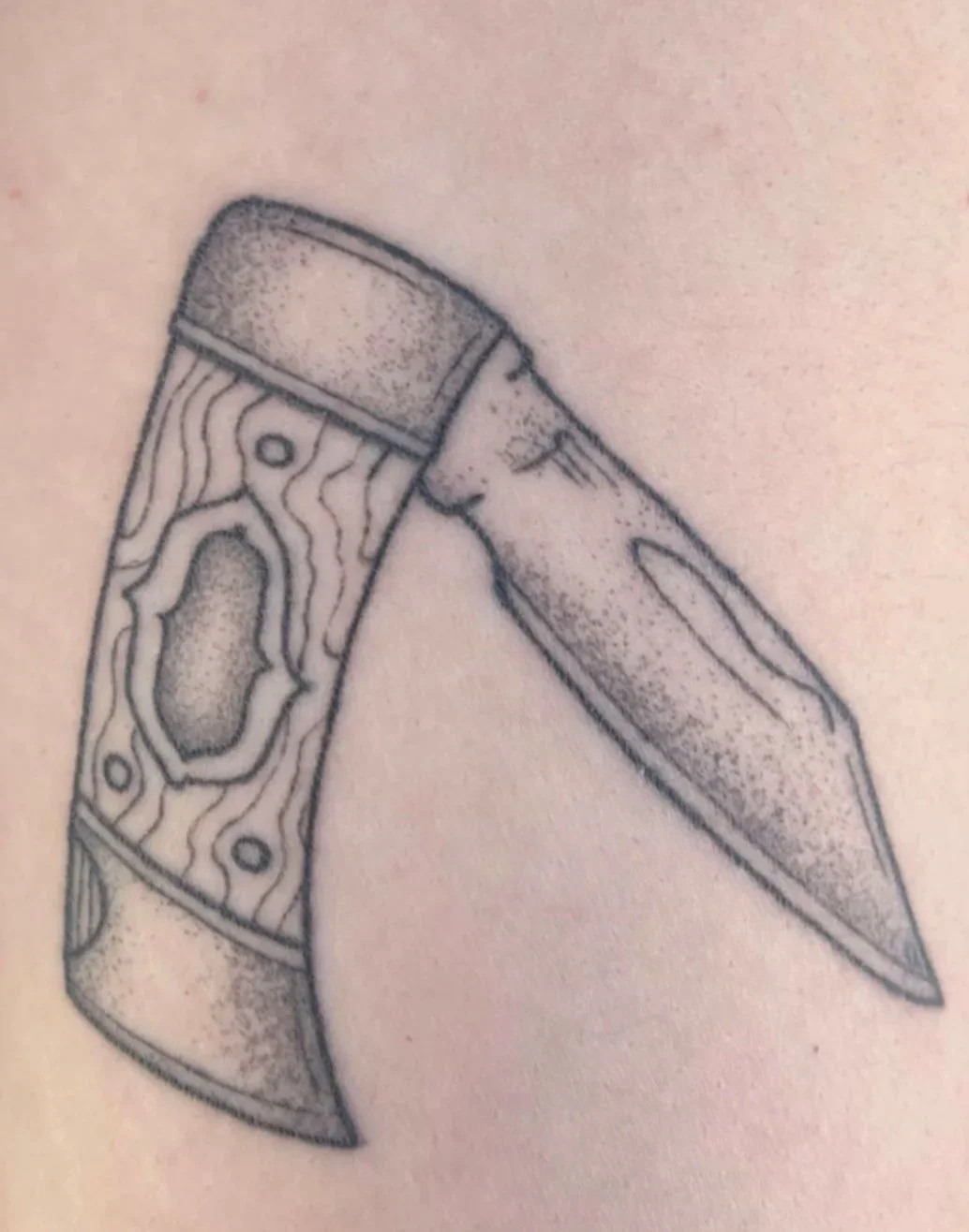 Tattoo of an axe with detailed wood grain texture and a sharp blade.