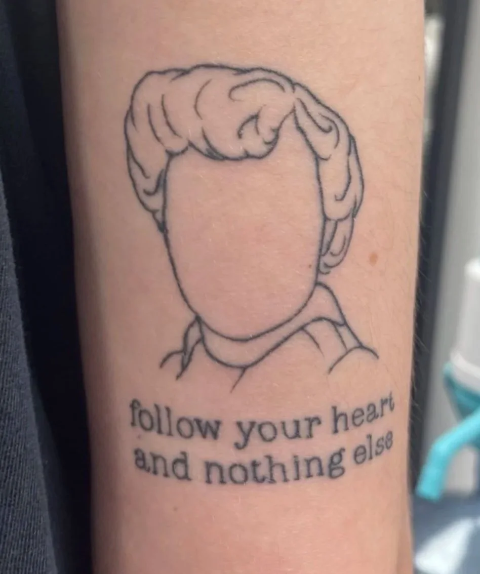 Tattoo of a faceless person with curly hair on upper arm. Text above says 'Healed'. Text below reads 'follow your heart and nothing else'.