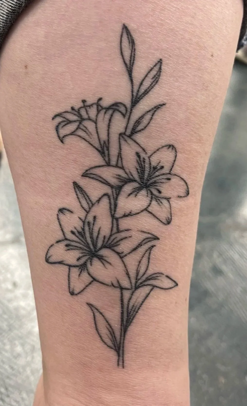 A black ink tattoo of lilies and leaves on a person's forearm, with the word 'Healed :)' overlayed on the top right.