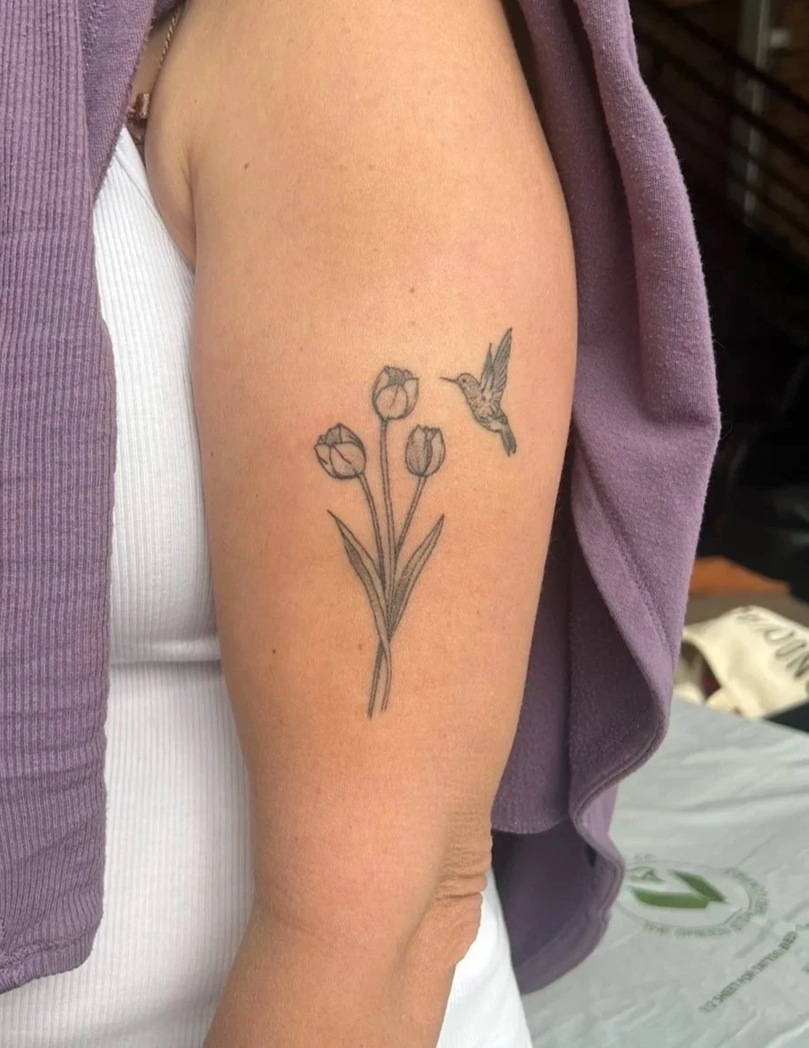 Tattoo of three tulips and a hummingbird on a woman's upper arm.