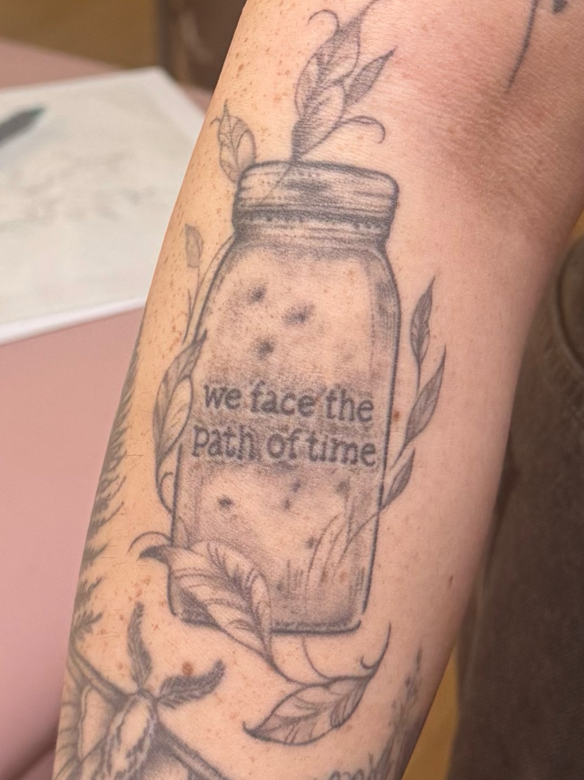 Tattoo of a salt shaker with the phrase 'we face the path of grief' inside, surrounded by leaves and decorative elements.