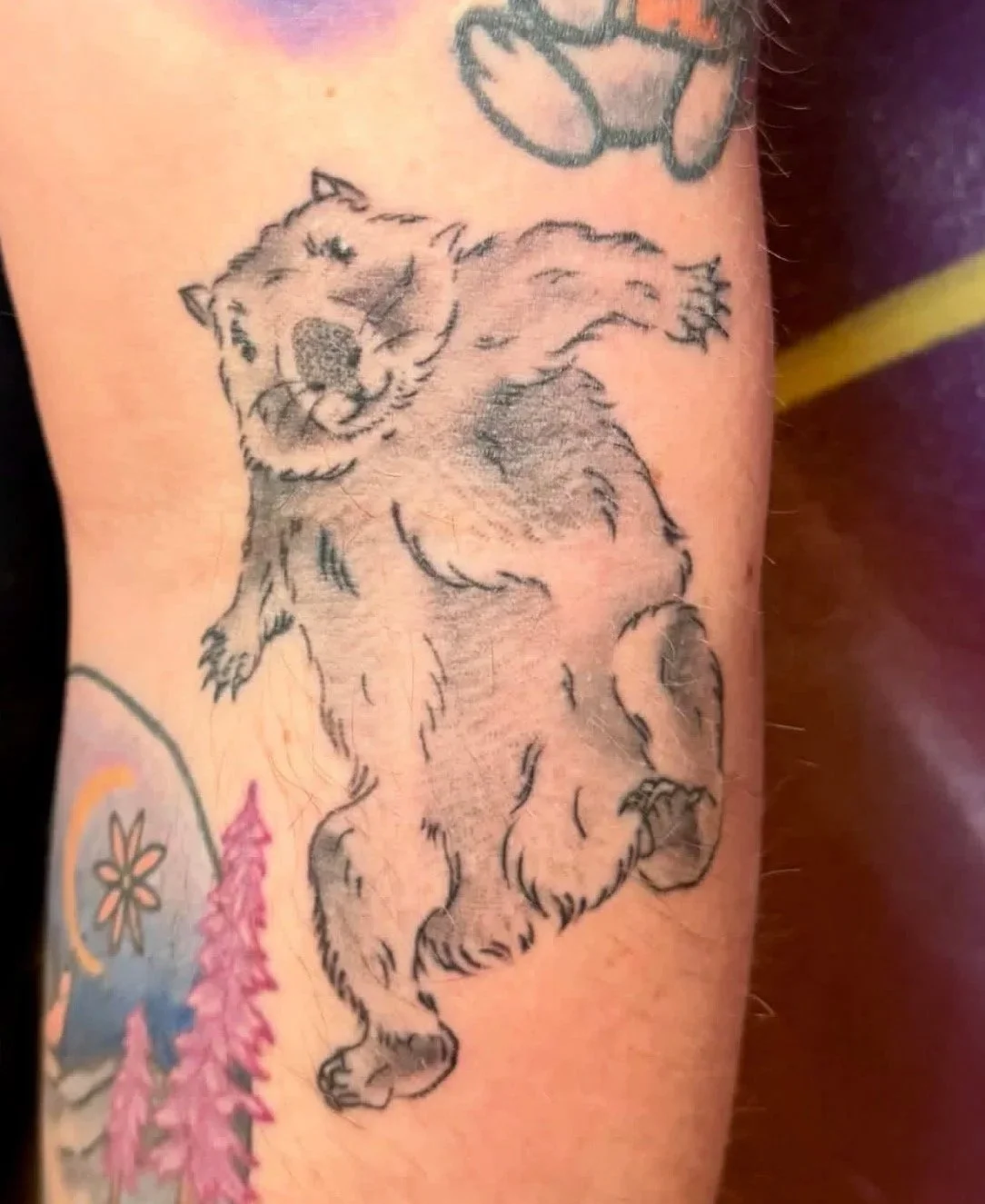 Tattoo of a smiling bear walking on its hind legs on a person's arm.