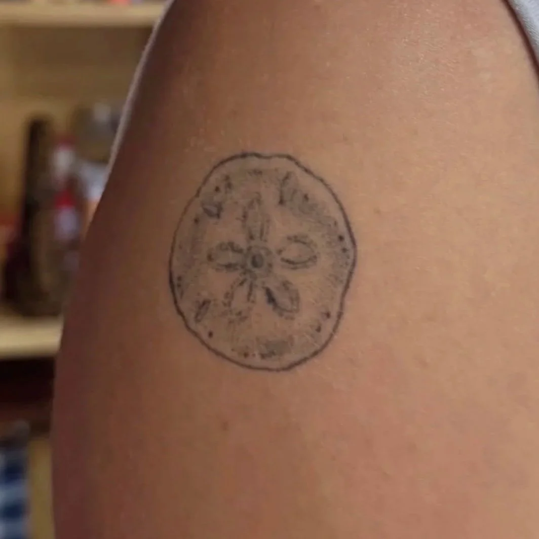 A close-up of a person's shoulder with a tattoo of a wheel or gear design.